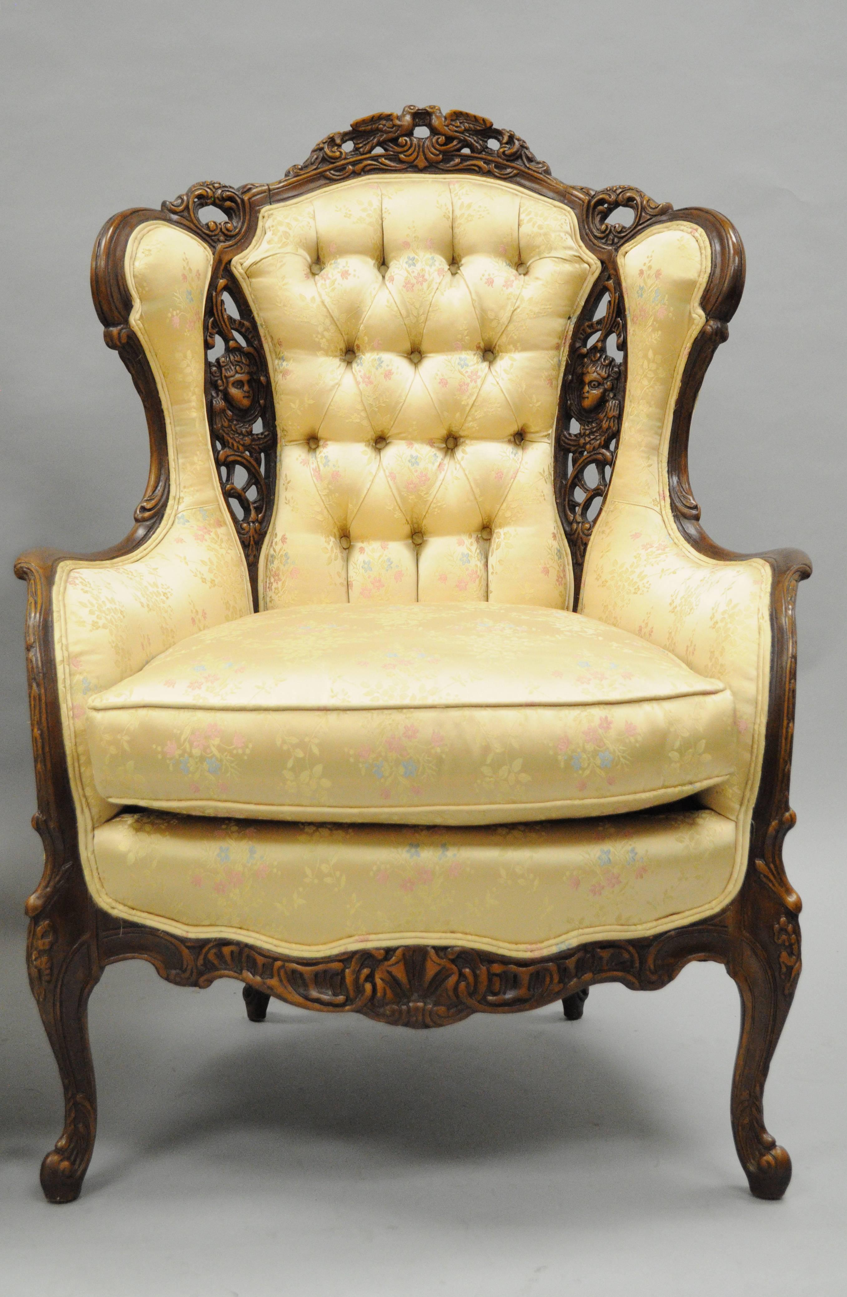 Pair of vintage carved wingback French, Louis XV style chairs with similar / complimentary carvings. Chairs feature solid carved wood frames with each chair having different carved figures, gold upholstery with rainbow stripes and blue and pink