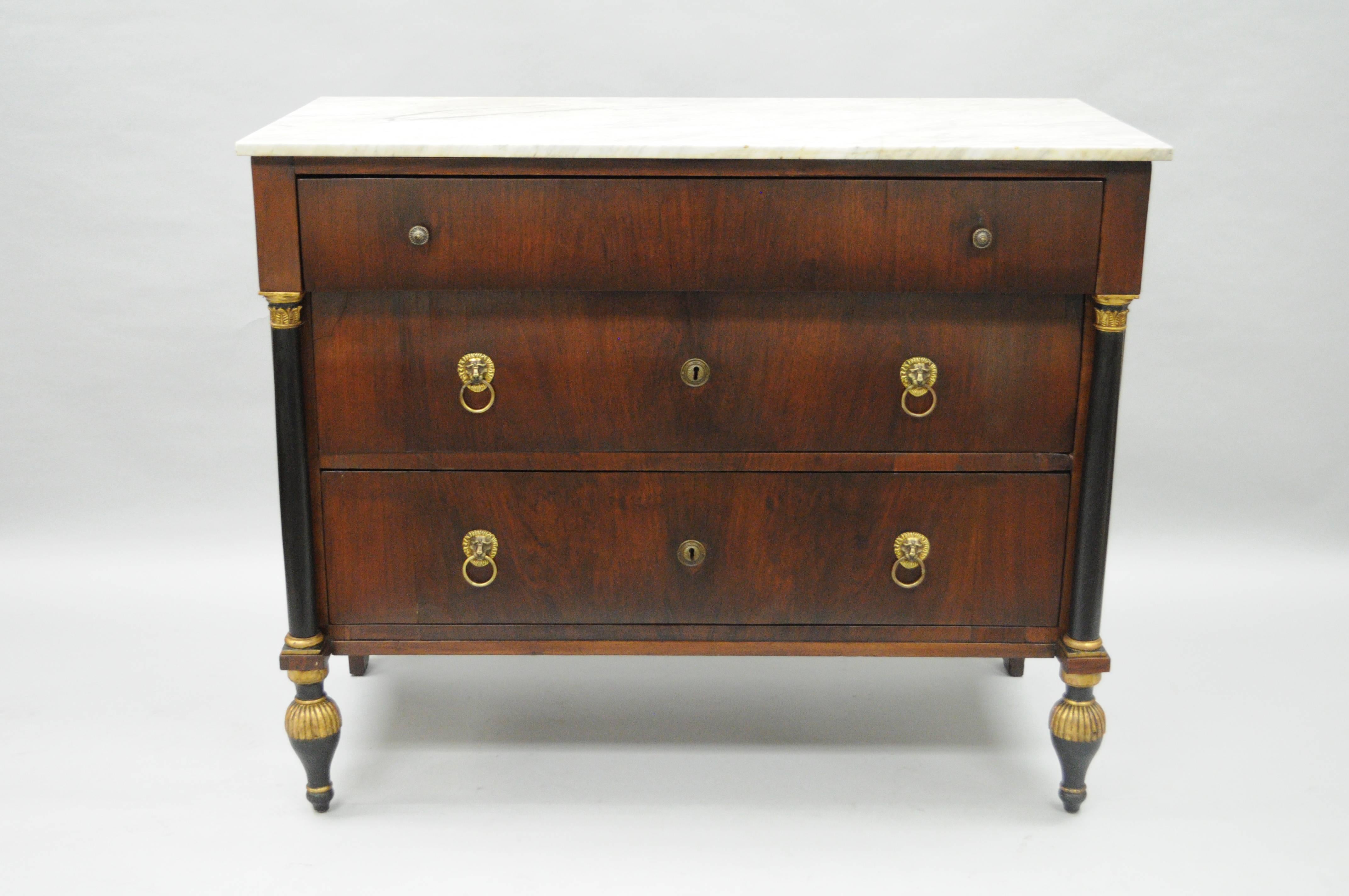 19th century antique French Empire style marble-top commode from the mid-1800s. Item features three hand dovetailed drawers, white Carrara marble top, brass lion drop pulls, dovetail joined case construction, ebonized and gold gilt columns and feet,