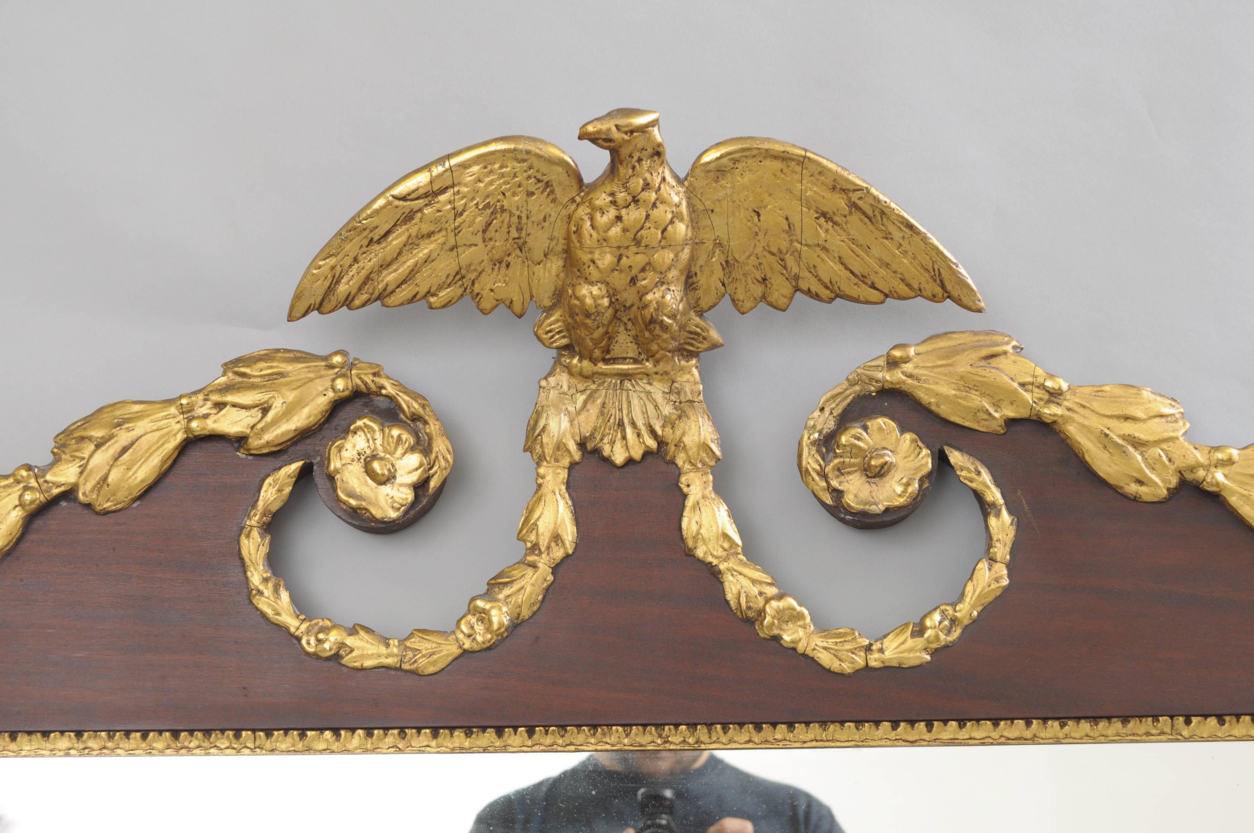 A horizontally oriented three-panel mahogany overmantel mirror with scrolling pediment centred with a mounted eagle finial with open wings and accented with a gold giltwood and gesso floral swag border with rosettes at the corners and pediment.