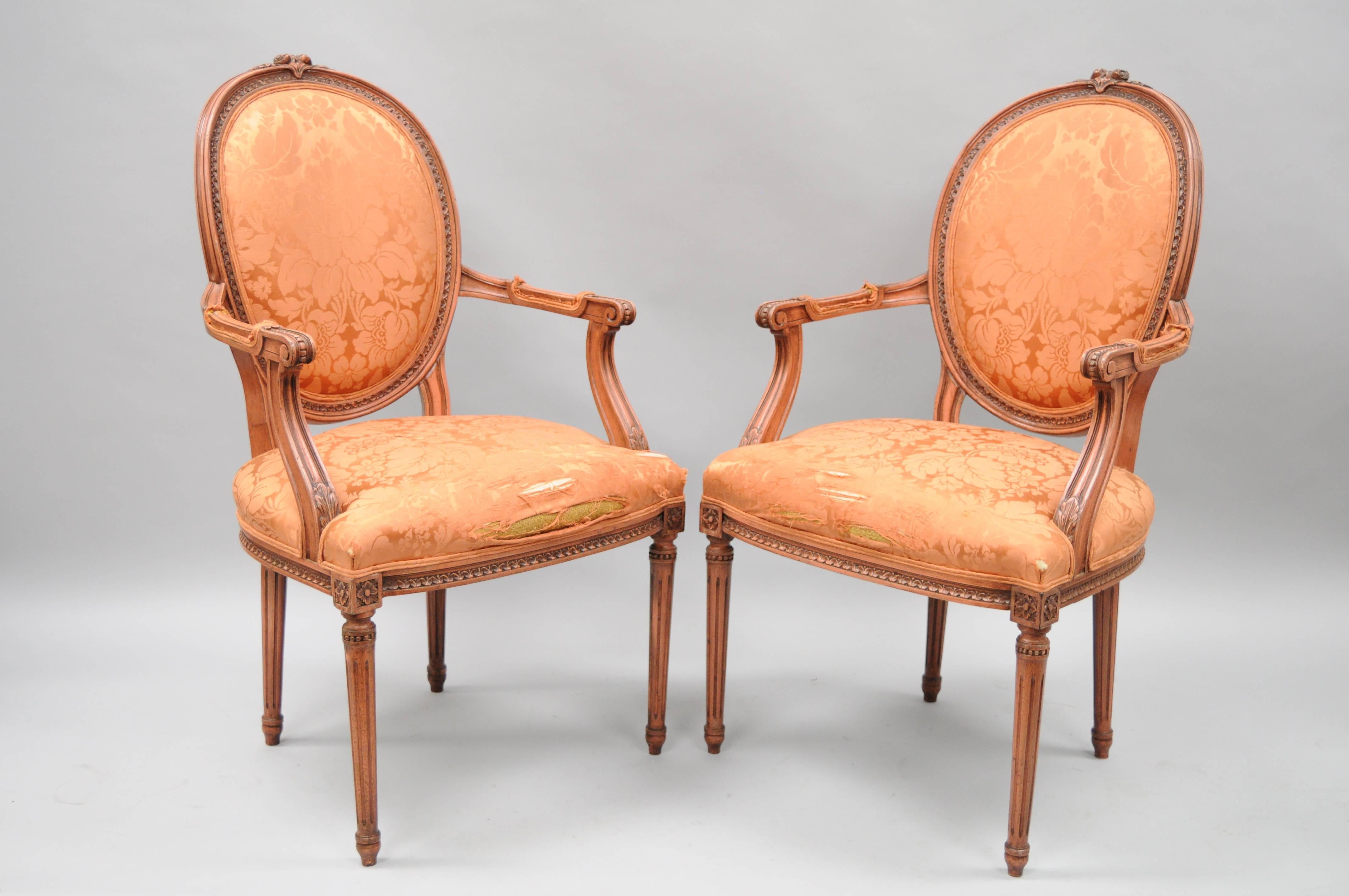 Pair of Vintage French Louis XVI style upholstered oval / medallion back dining armchairs with pink distress painted finish. Item features solid carved wood frames, oval backs with floral carved crest, upholstered armrests, reed carved and tapered