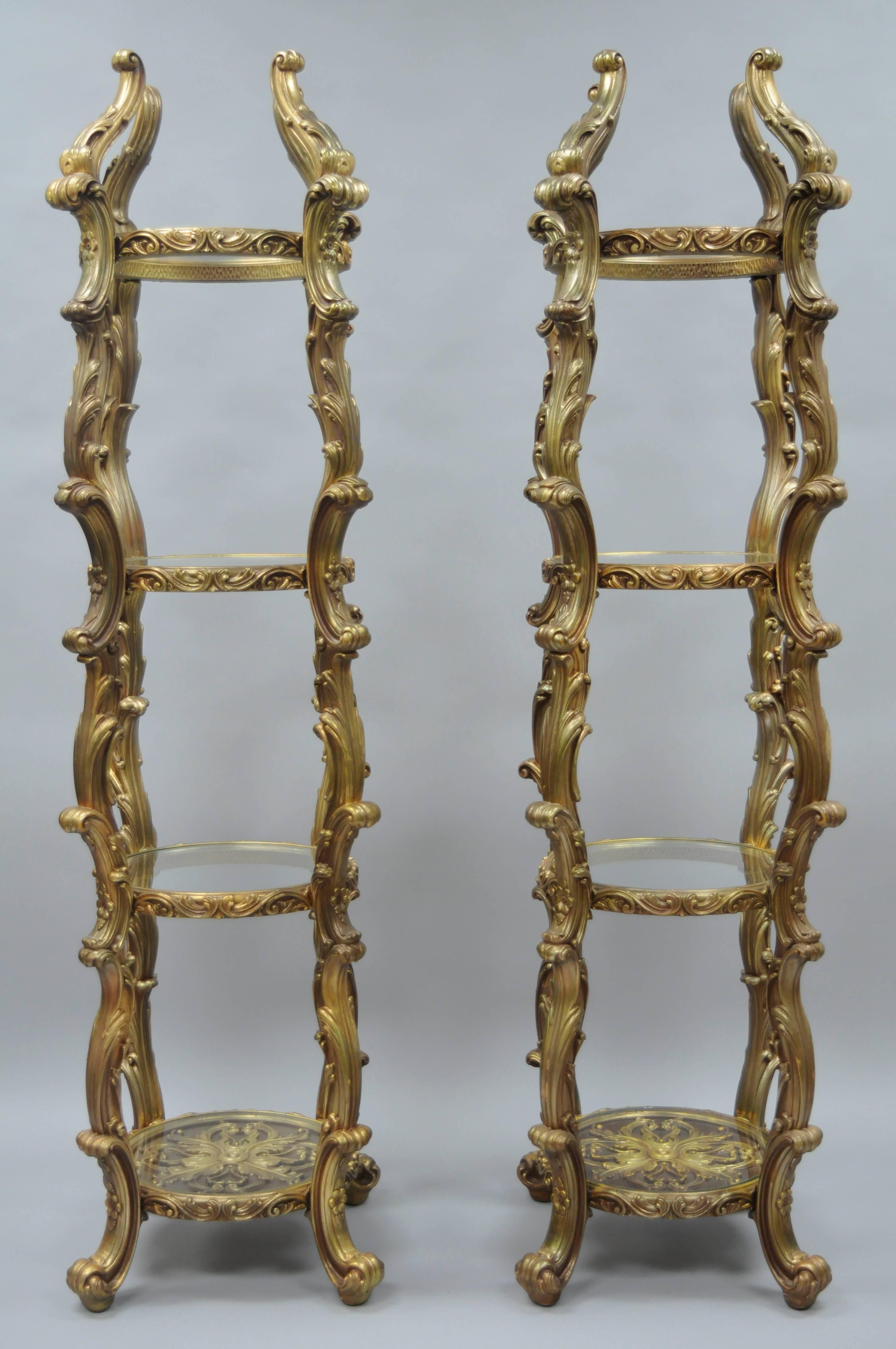 Pair of vintage gold Hollywood Regency Syroco etagere curios. The pair features nice round narrow forms, fancy acanthus leaf design molded frames, four round glass shelves with the lowest shelf having ornate detailing under the glass and an
