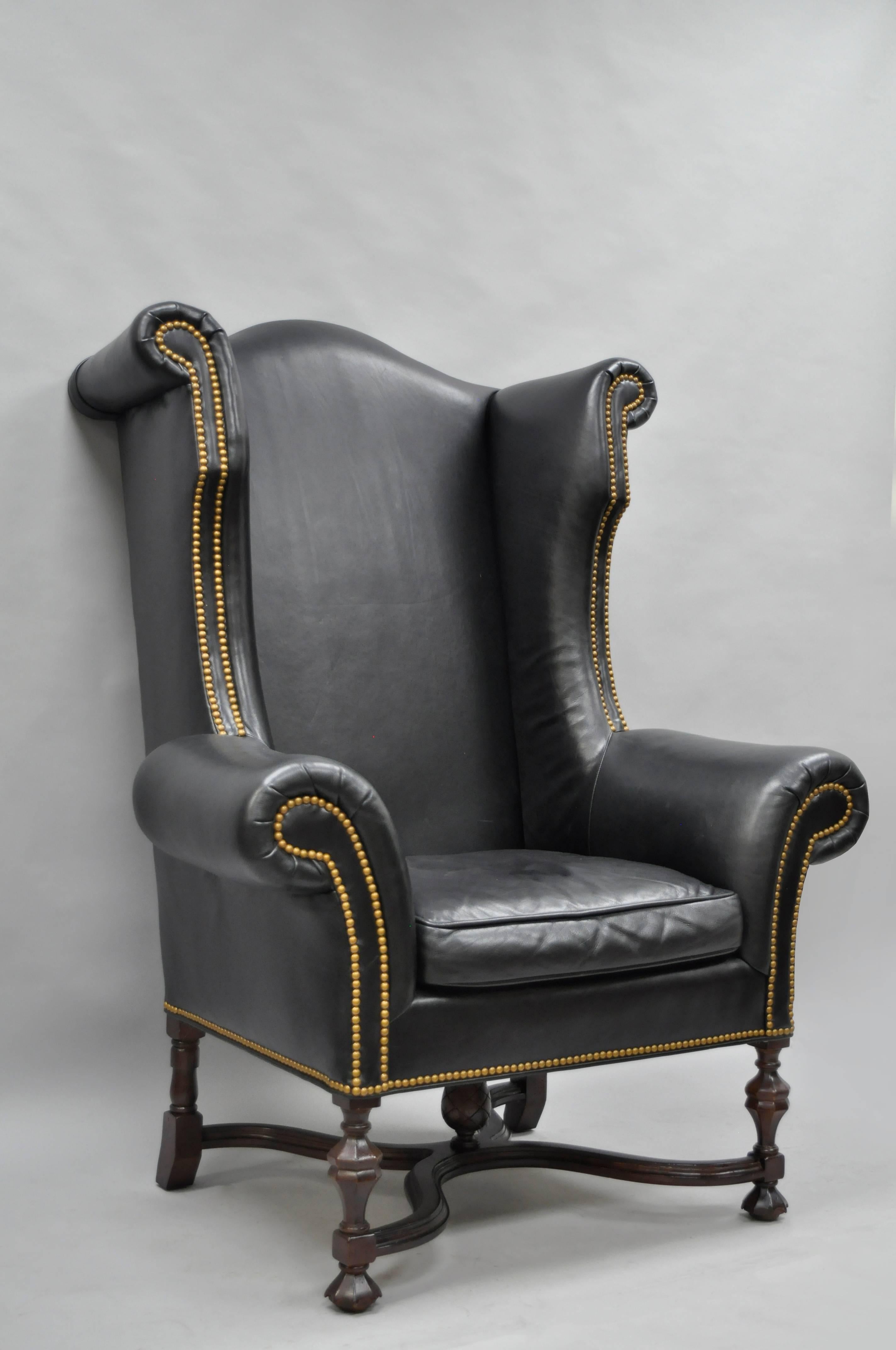 Large and Stately William and Mary black leather wingback chair (Item H4274-20) by Lee Jofa. Item features a oversize frame with rolled arms and back, brass nailhead trim throughout, solid carved wood stretcher base with carved acorn/pineapple