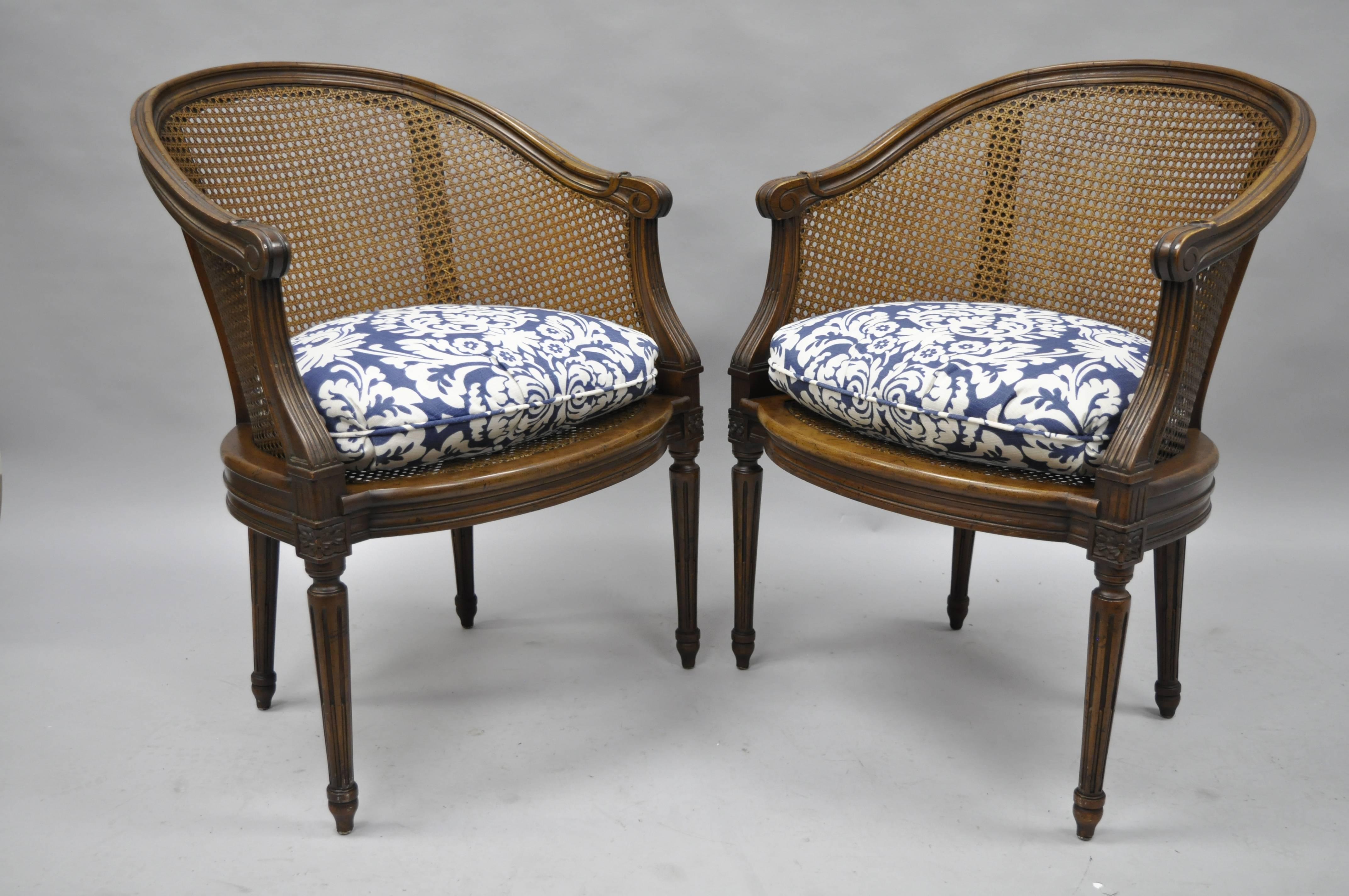 Elegant pair of vintage French Louis XVI style walnut and cane barrel back chairs by Heritage Furniture, circa 1960s. Chairs feature solid wood construction, distressed finish, cane seat and back, later added loose cushions, original label, tapered