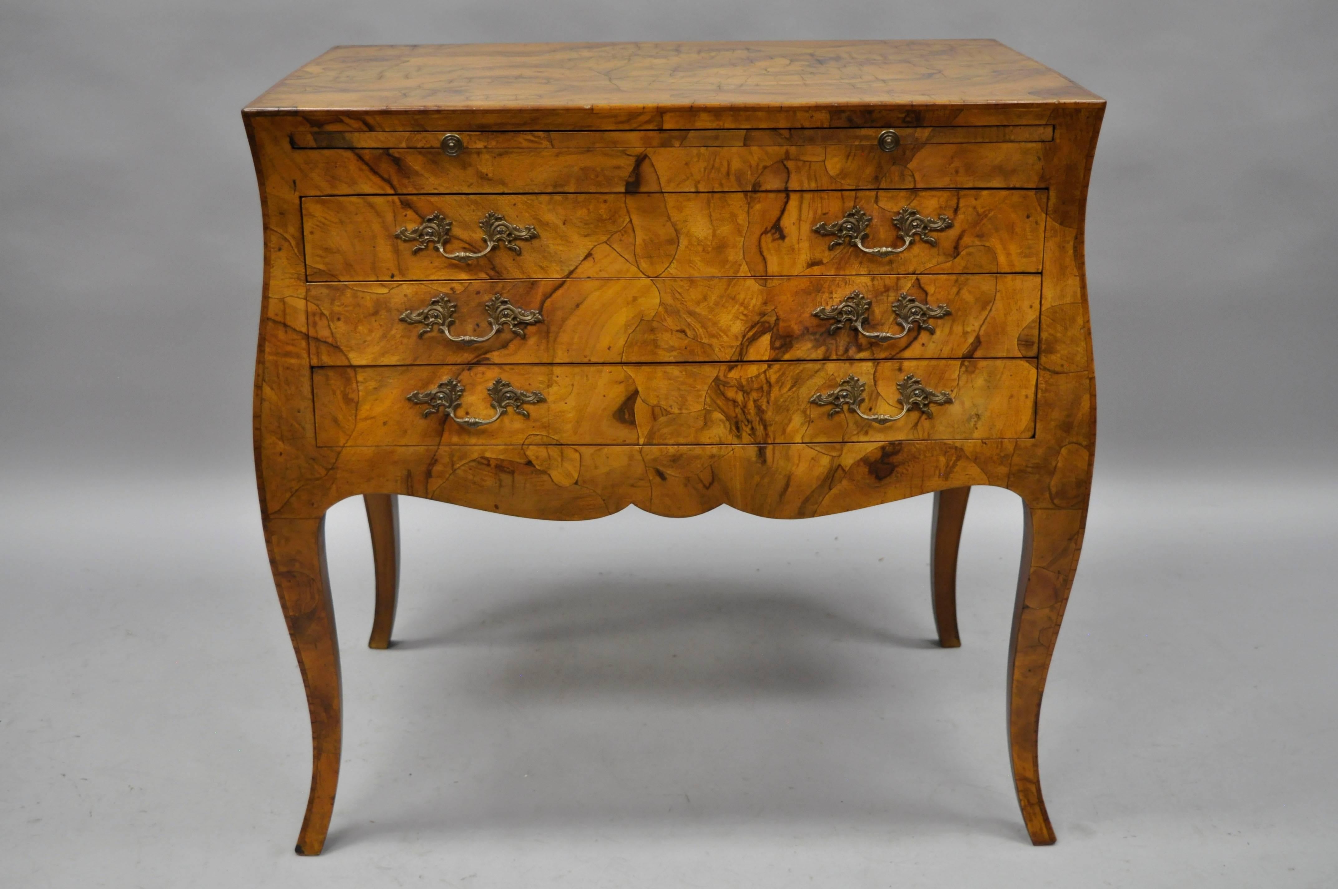 Stunning Italian olivewood French Louis XV style commode. Item features beautiful bookmatched patchwork olive wood veneers, pull-out surface, ornate brass handles, three drawers, shapely cabriole legs, and is finished all the way around. Item
