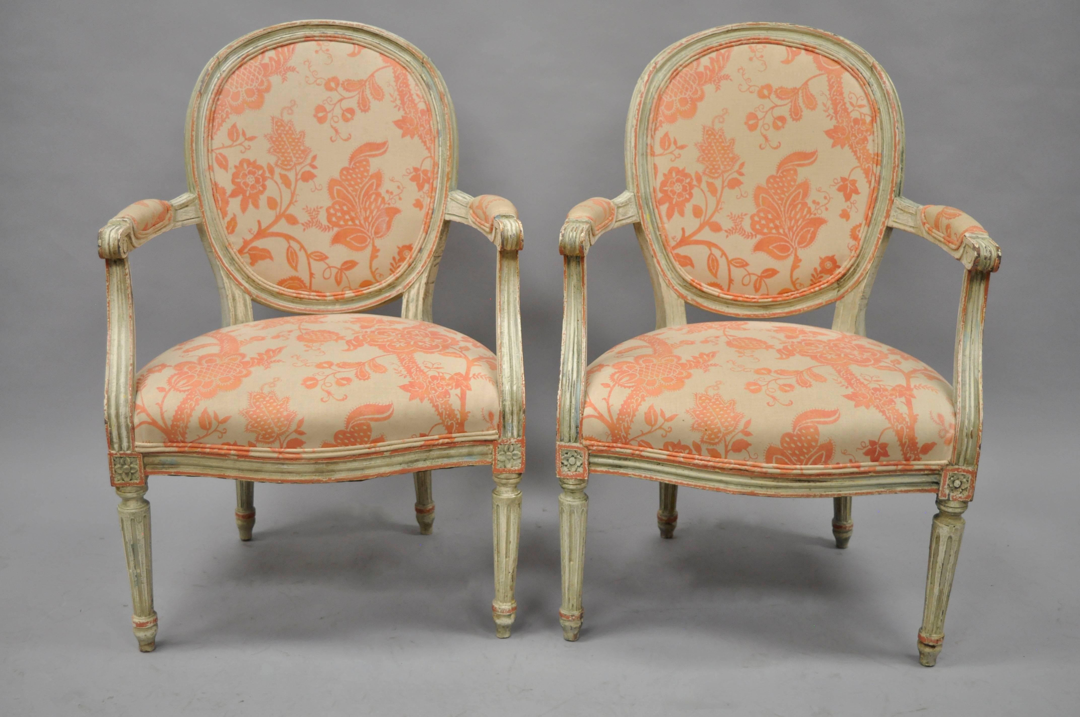 Early 20th century pair of French, Louis XVI style Fauteuil armchairs. Chairs feature solid carved wood frames, medallion backs, stretcher supported backrest, reed and tapered legs, distressed/antiqued painted finish in cream, green and peach.