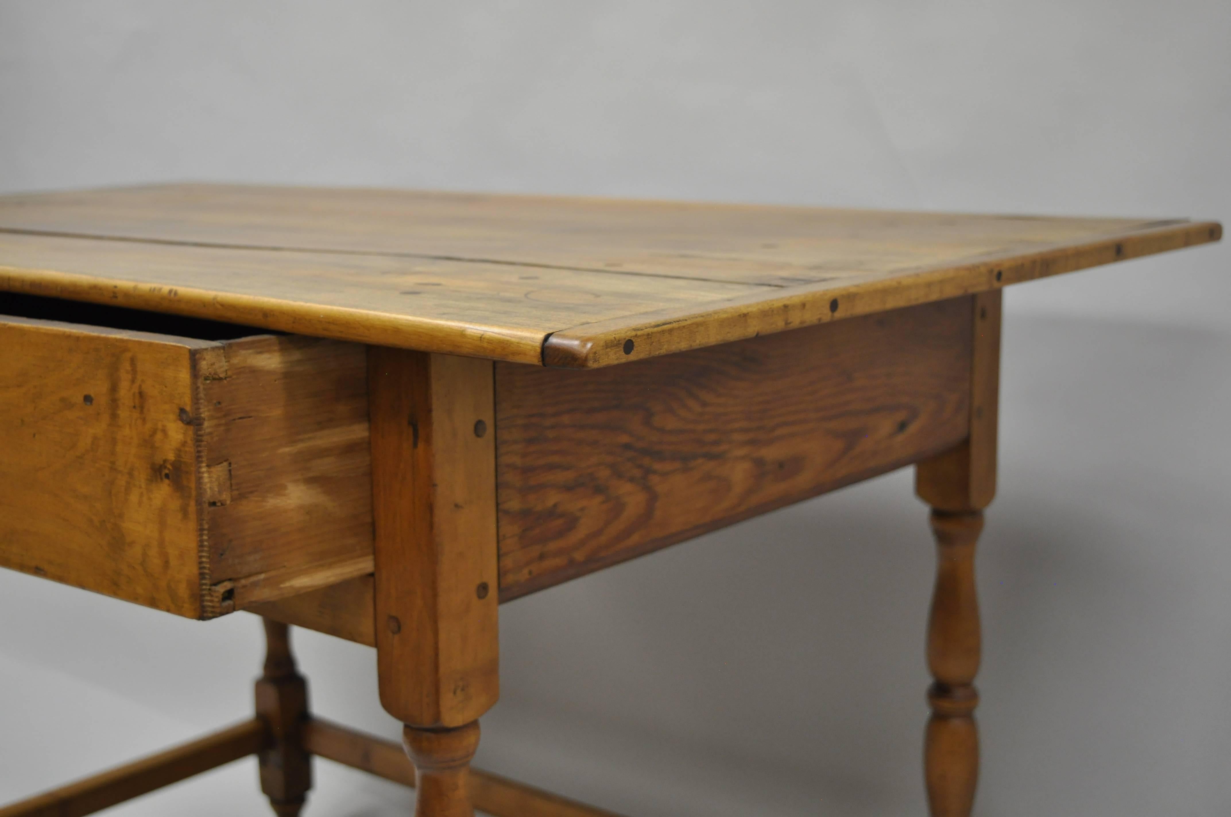Antique American maple and pine wood tavern table with drawer, circa early 1800s. Item features a single dovetailed drawer, turn carved legs, wooden pin construction, stretcher base, and elongated old scrubbed plank top with various dowels and pins.