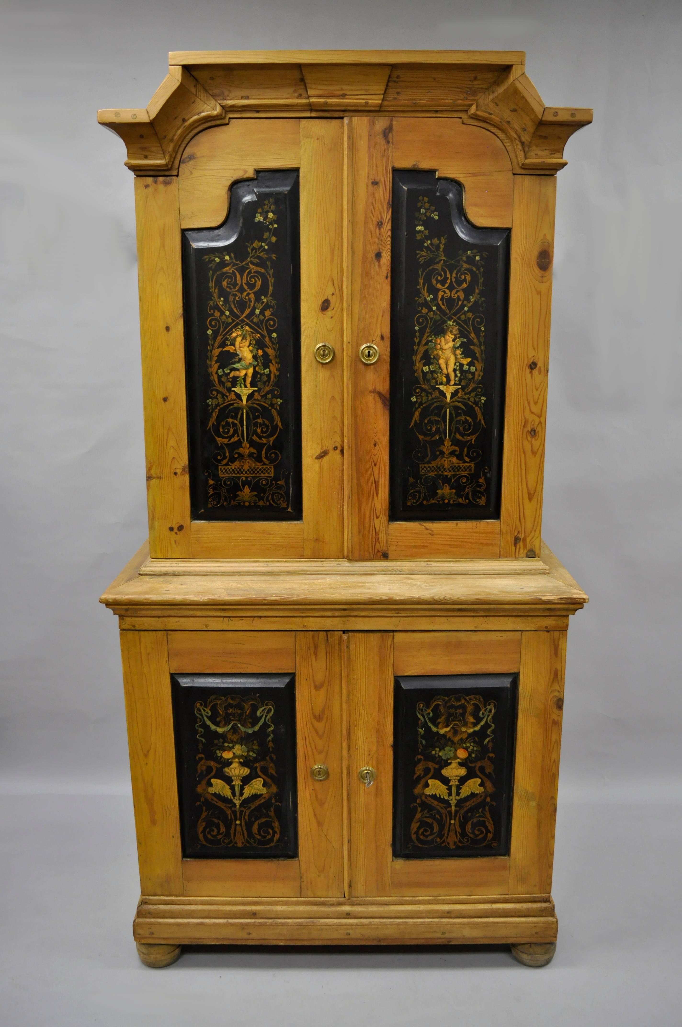 Primitive French Country neoclassical style cherub painted pine wood cabinet. Item features a distressed solid pine wood two part construction, four swing cabinet doors with hand-painted black panels. The upper doors feature dancing cherubs and