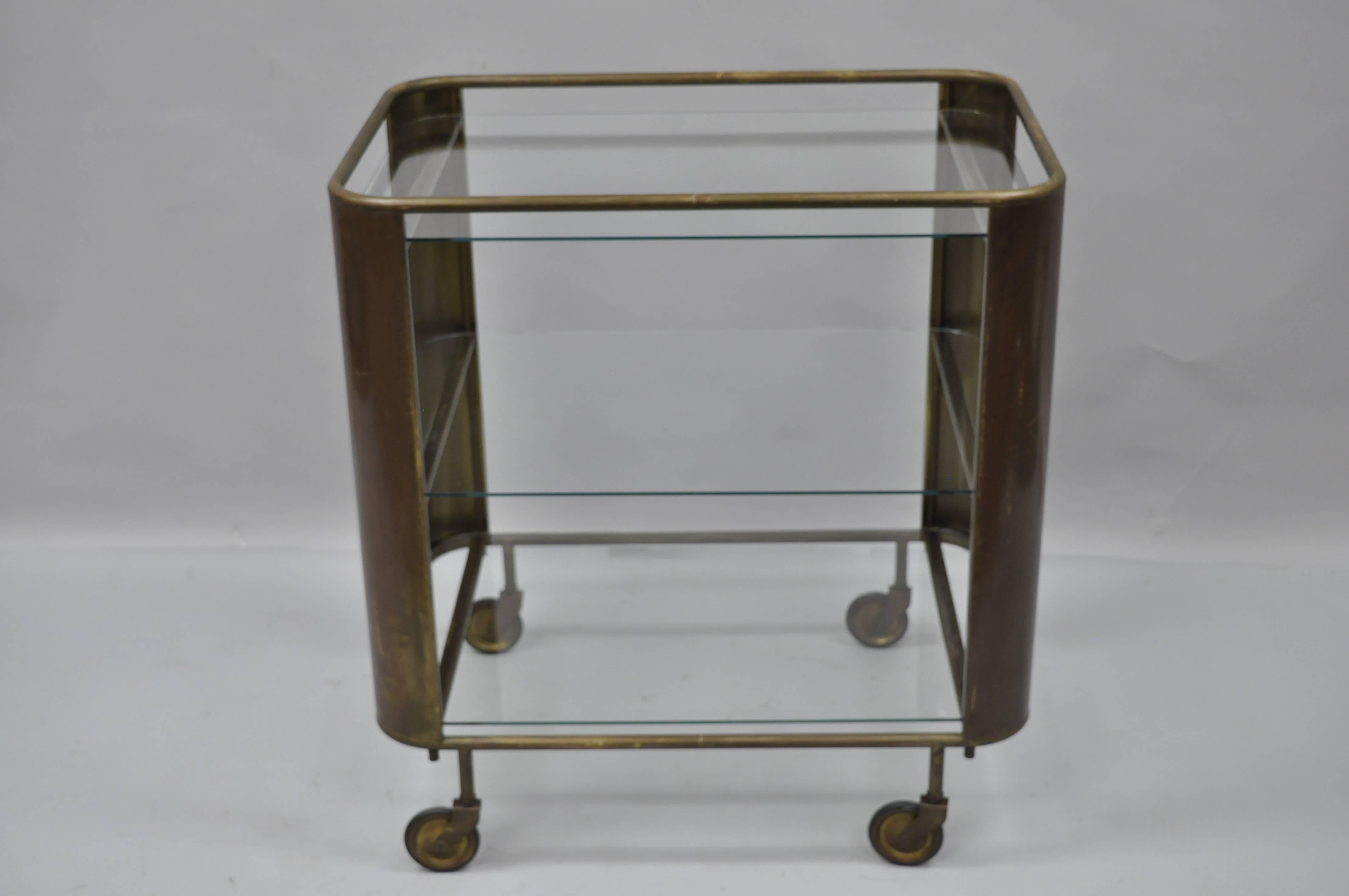 Vintage Italian Mid Century Modern burnished brass and glass modernist bar cart trolley. Item features a antiqued/burnished brass frame, three floating glass shelves and rolling casters. Attractive aged patina to brass. Very unique bar cart.