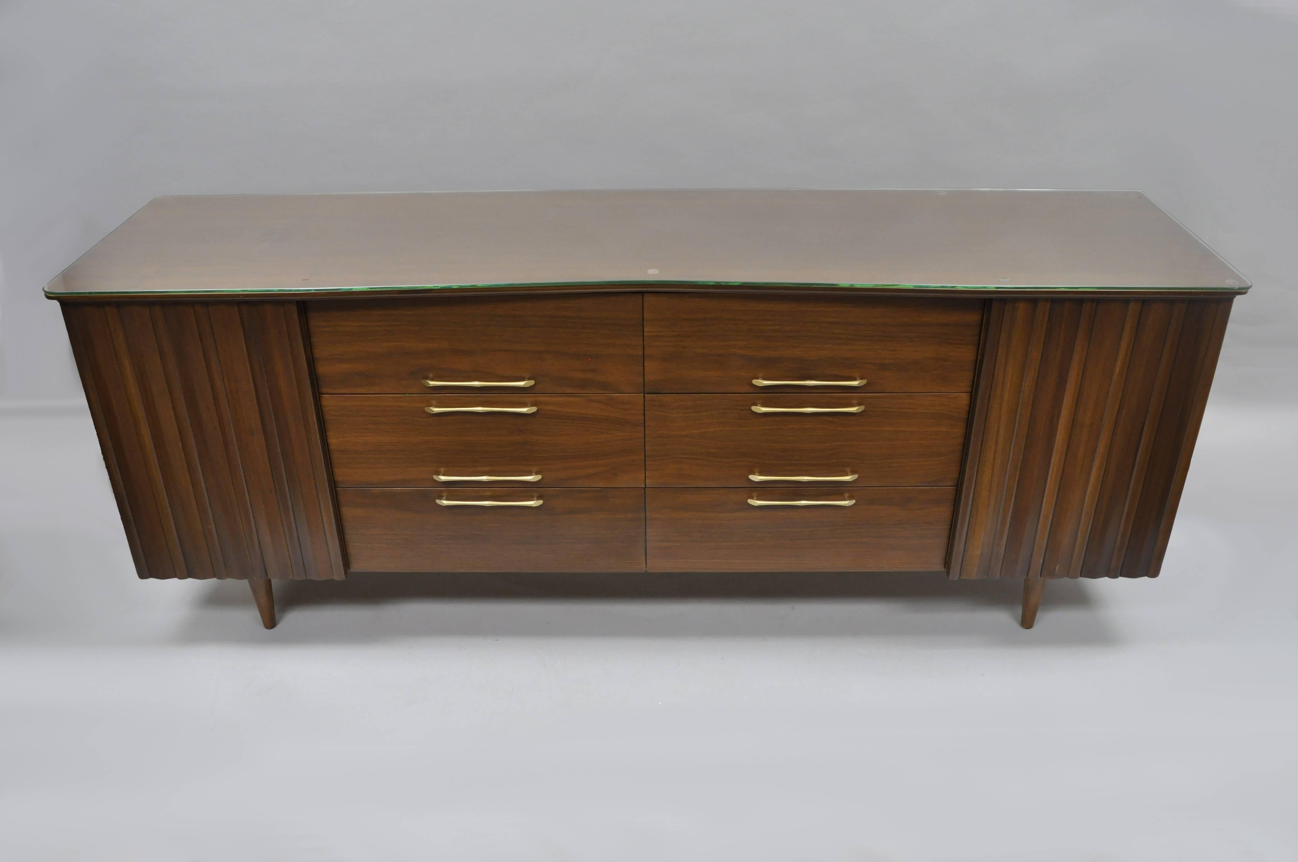 Superb Vintage midcentury American modern walnut long dresser. Original owners had dresser professionally refinished inside and out with custom angled glass top added. Item features two sculptural walnut doors, 12 dovetailed drawers, shaped top,