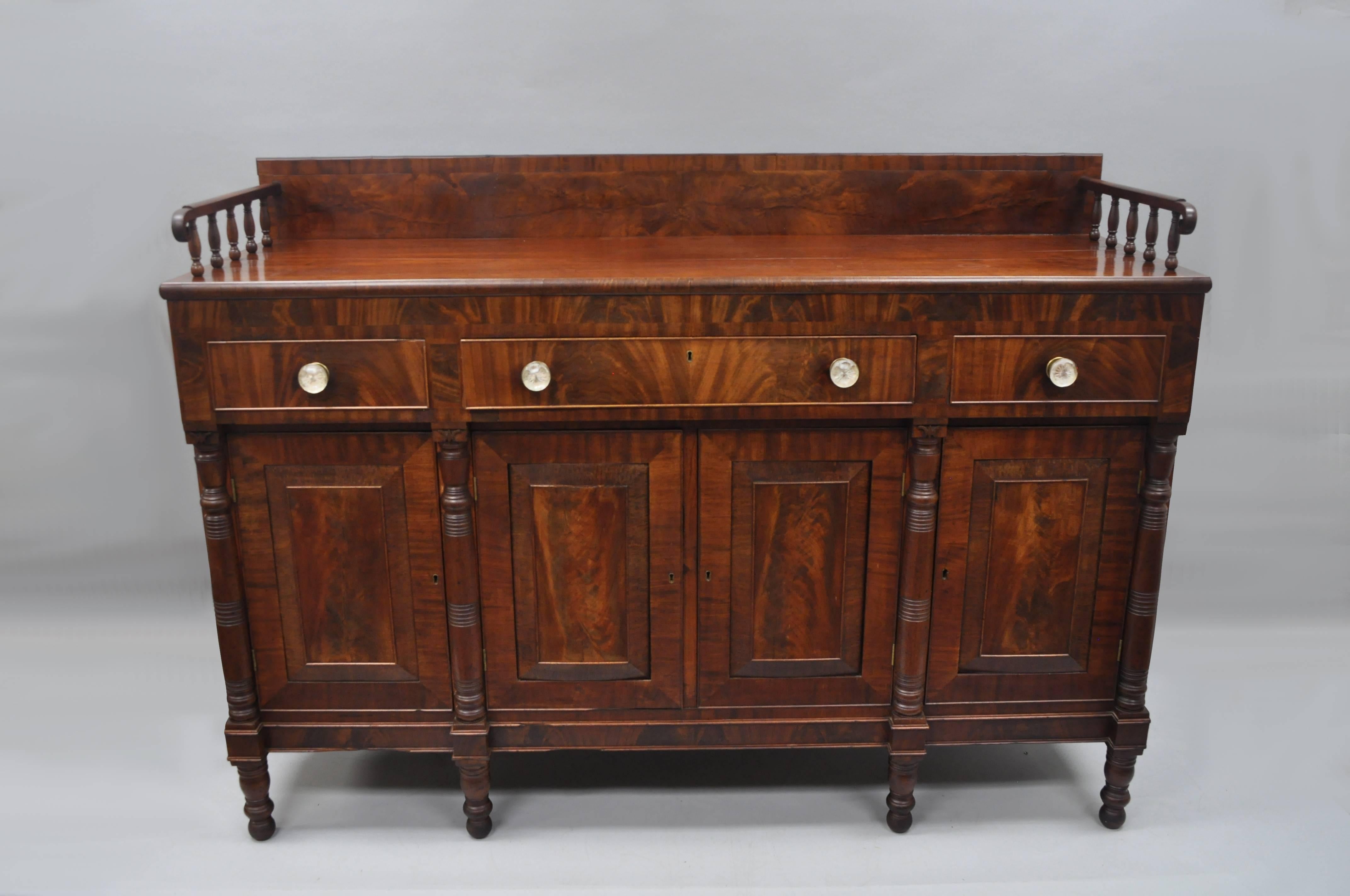 Early 19th Century Large Antique American Empire Sideboard in Crotch Flame Mahogany with 2 pull out surfaces on the sides. Item features beautiful crotch mahogany wood veneer, tall back splash with spindle sides, glass knob pulls, turn carved legs