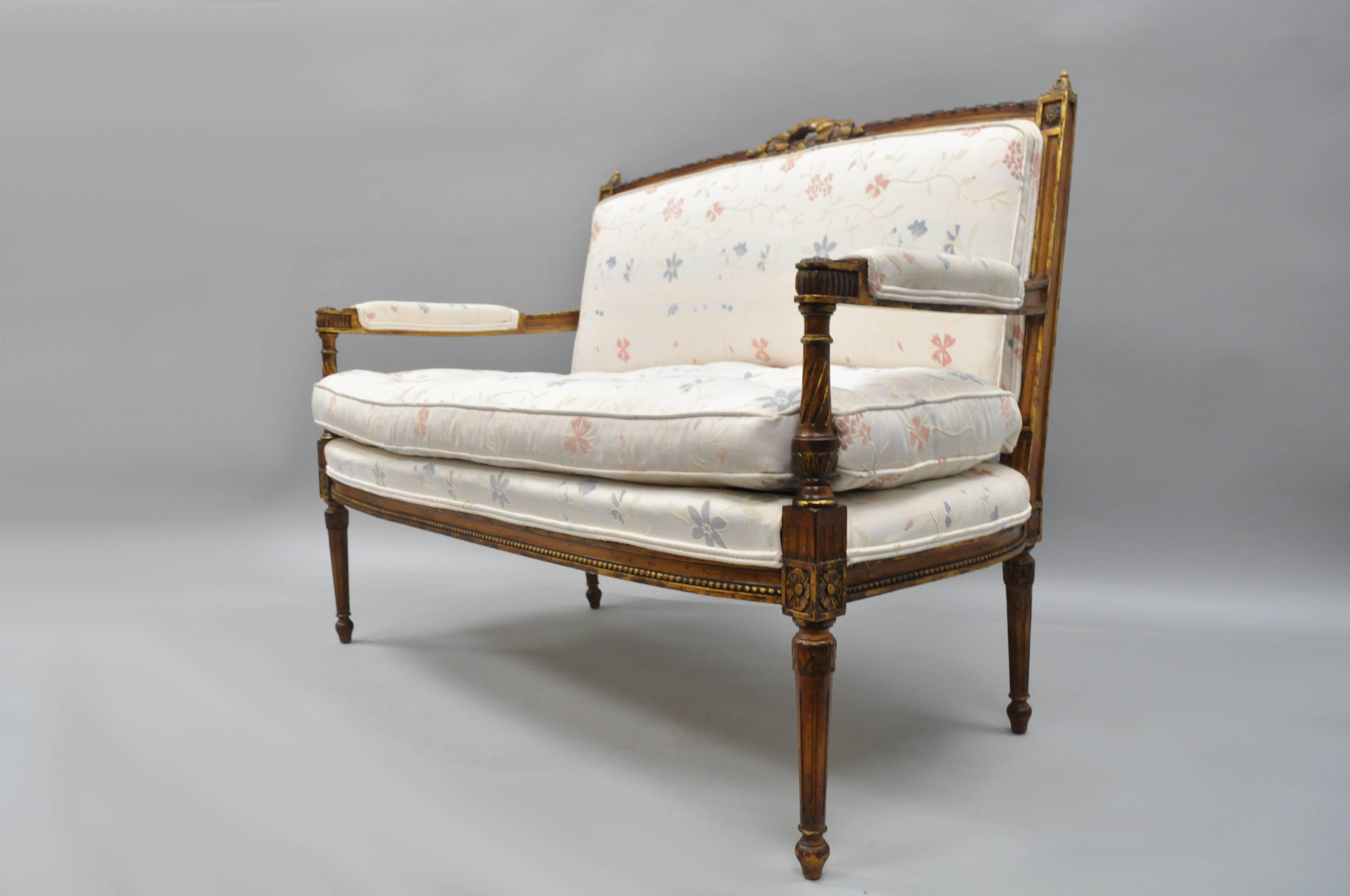 Vintage French Louis XVI style gold settee, circa mid-20th century. Settee features a ribbon carved crest, rectangular back, solid wood frame, upholstered armrests, floral print fabric with tufted seat, reed and tapered legs, loose cushion, and
