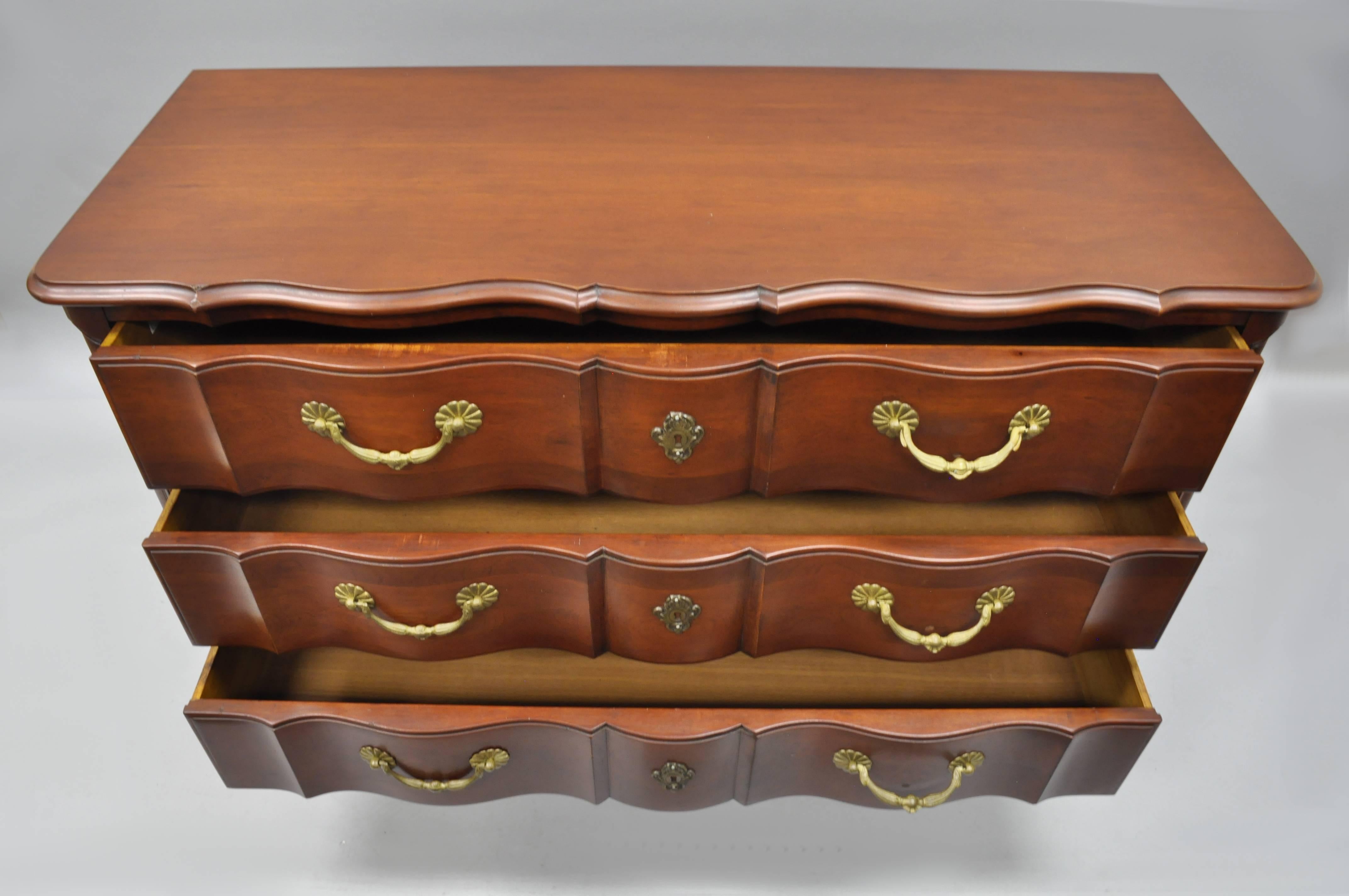 Vintage French Country / Louis XV style bachelor chest by John Widdicomb. This cherry wood commode features beautiful wood grain, three dovetail constructed drawers, solid brass hardware, cabriole legs, shaped front, and quality American