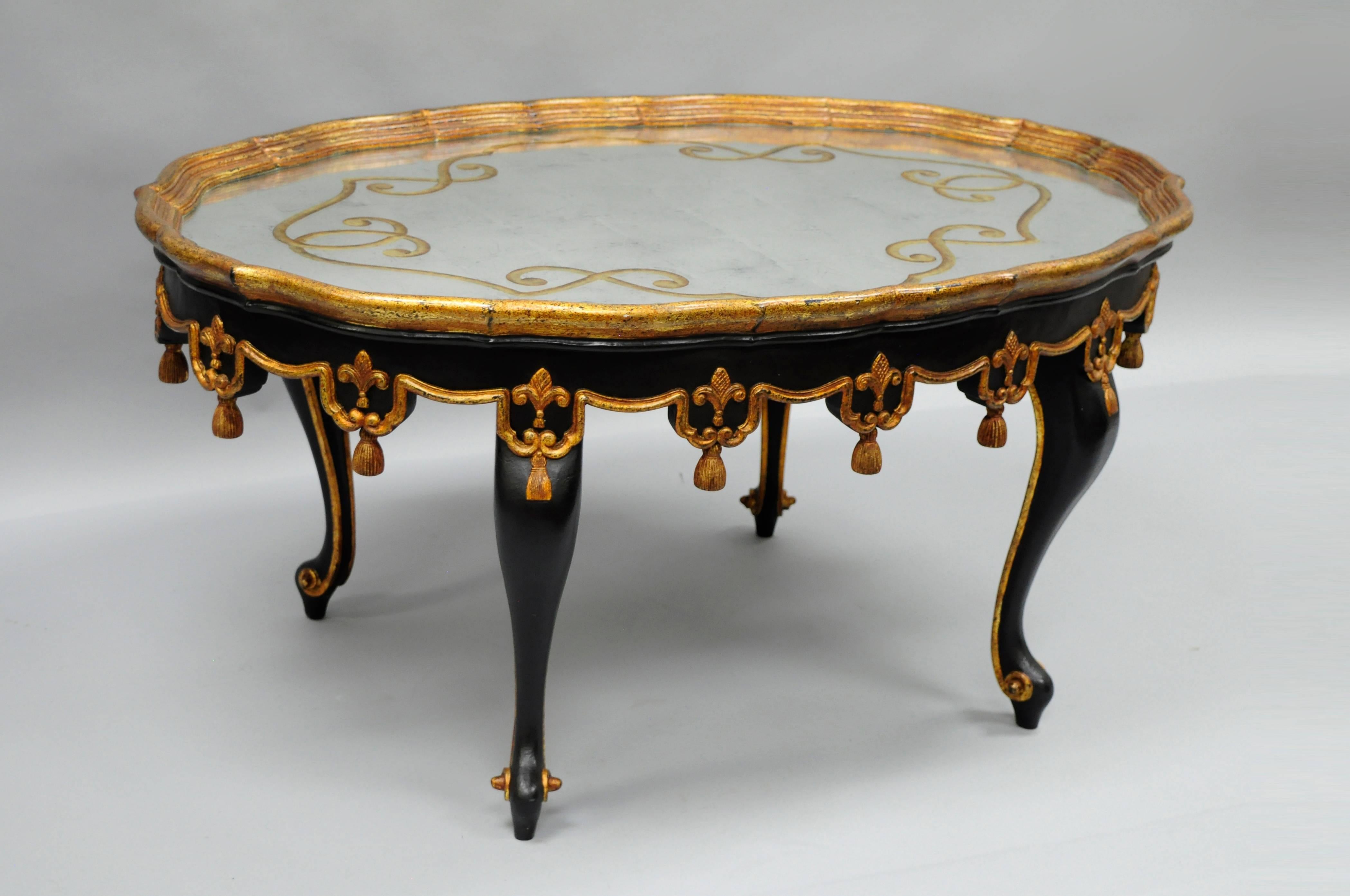 Gorgeous black and gold gilt coffee table in the Maison Jansen / French Louis XVI style attributed to John Richard. Table features a carved wood tassel skirt, scrolling cabriole legs, and a beautiful églomisé decorated mirrored glass top.