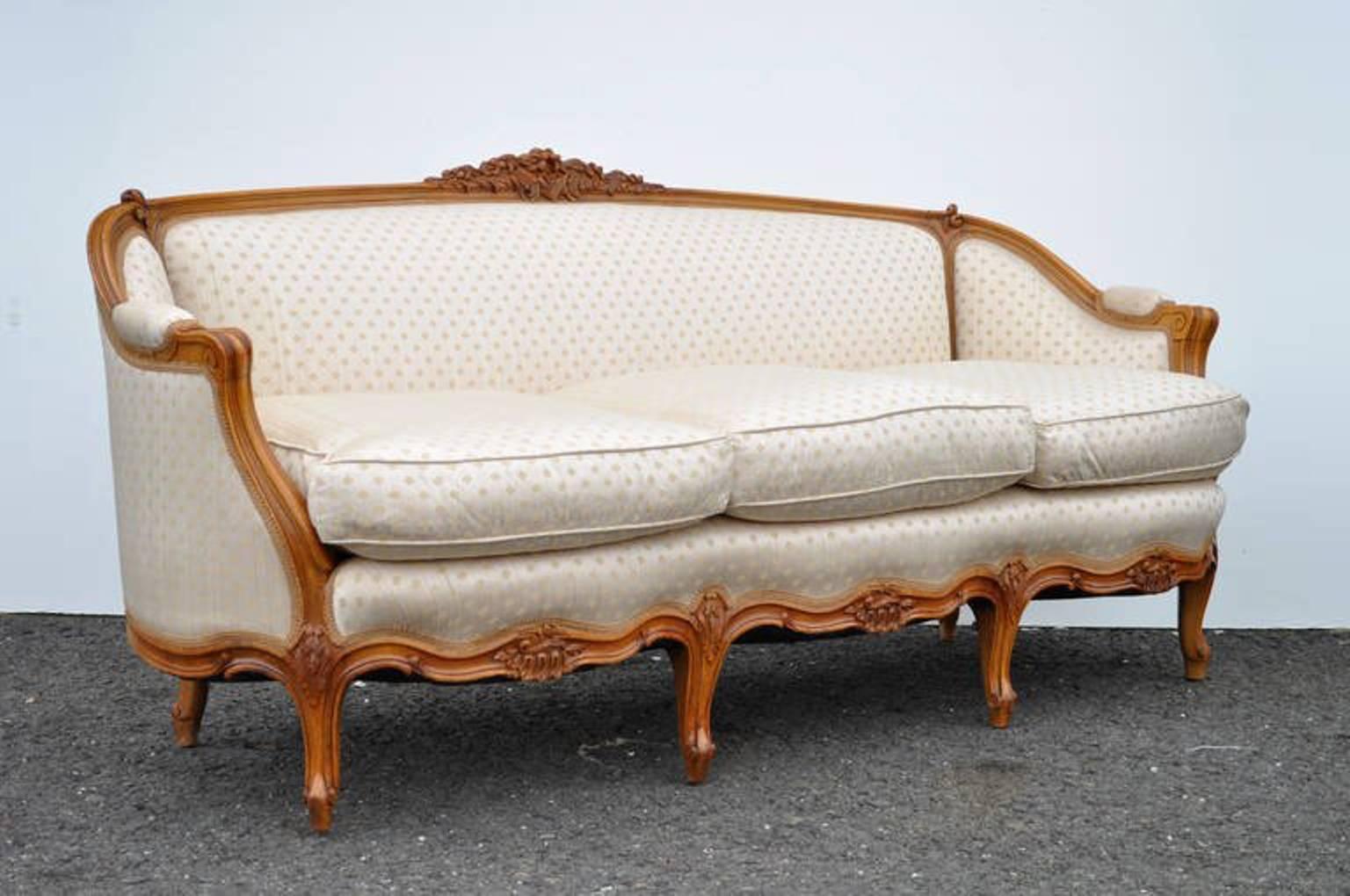 Superbe canapé français vintage en noyer sculpté de style Louis XV. Cet article présente des accents floraux magnifiquement sculptés, des bras en volute et six pieds cabriole, ainsi qu'un joli revêtement beige et or à motif de trèfle et des coussins