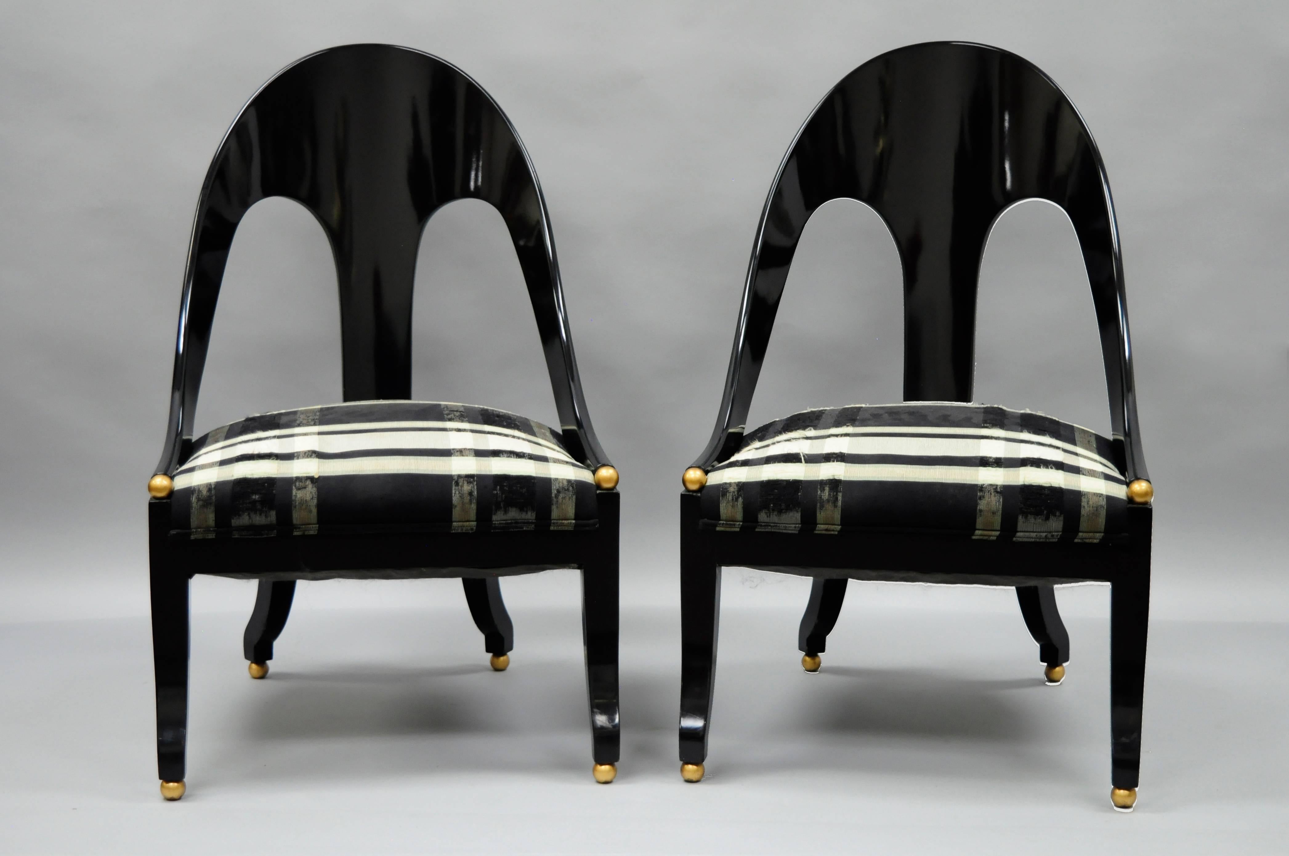 Pair of black lacquered spoon back slipper chairs designed by Michael Taylor for Baker in the neoclassical style. The chairs feature a sleek elegant design with a gloss black lacquered finish, and gold toned orbs at the ends of the armrests and