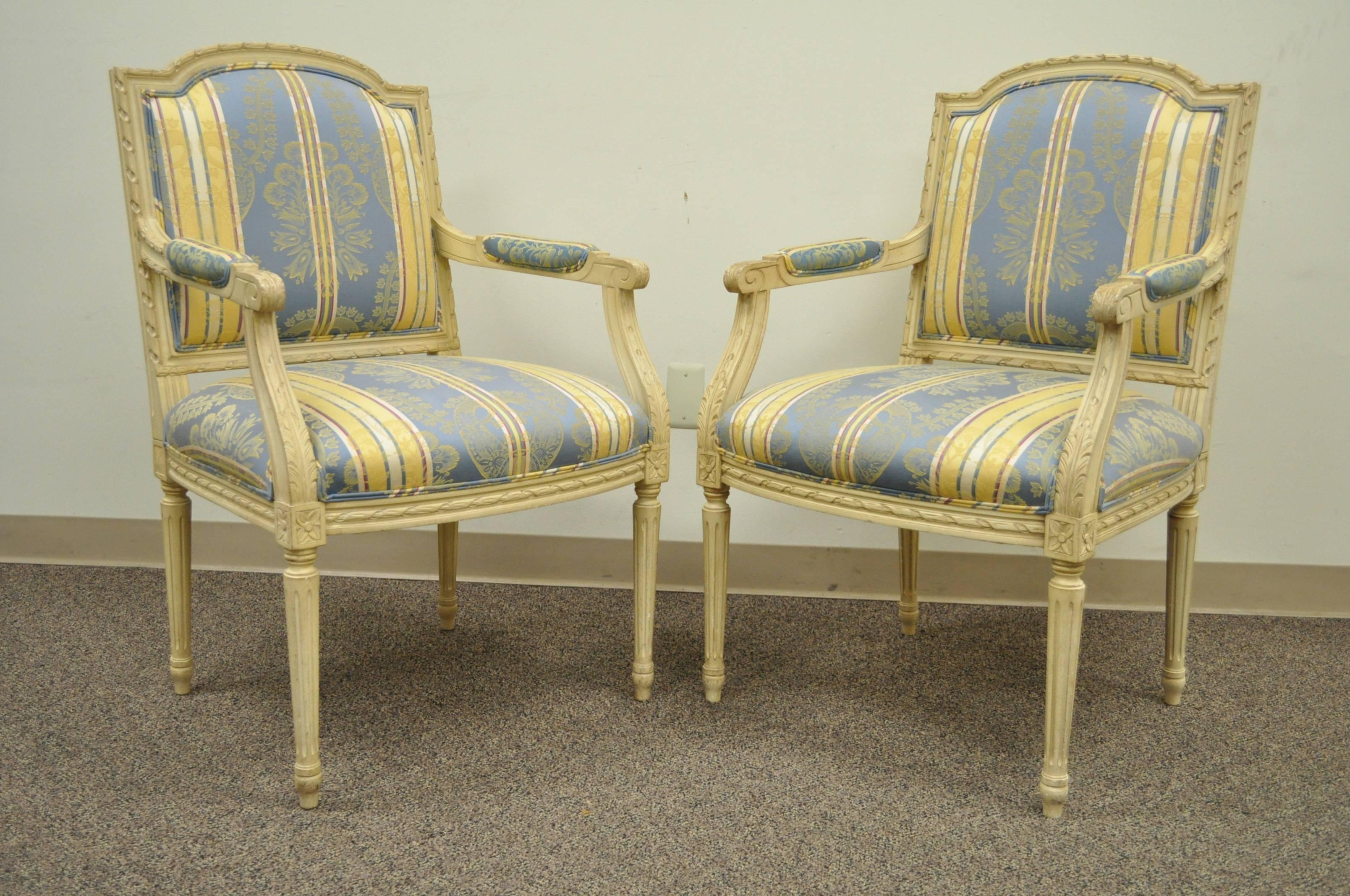 Pair of 20th Century French Louis XVI style armchairs with finely carved floral and ribbon form accents, scroll form arms, and reeded and tapered column form legs. The chairs are upholstered in an absolutely lovely blue and yellow striped fabric