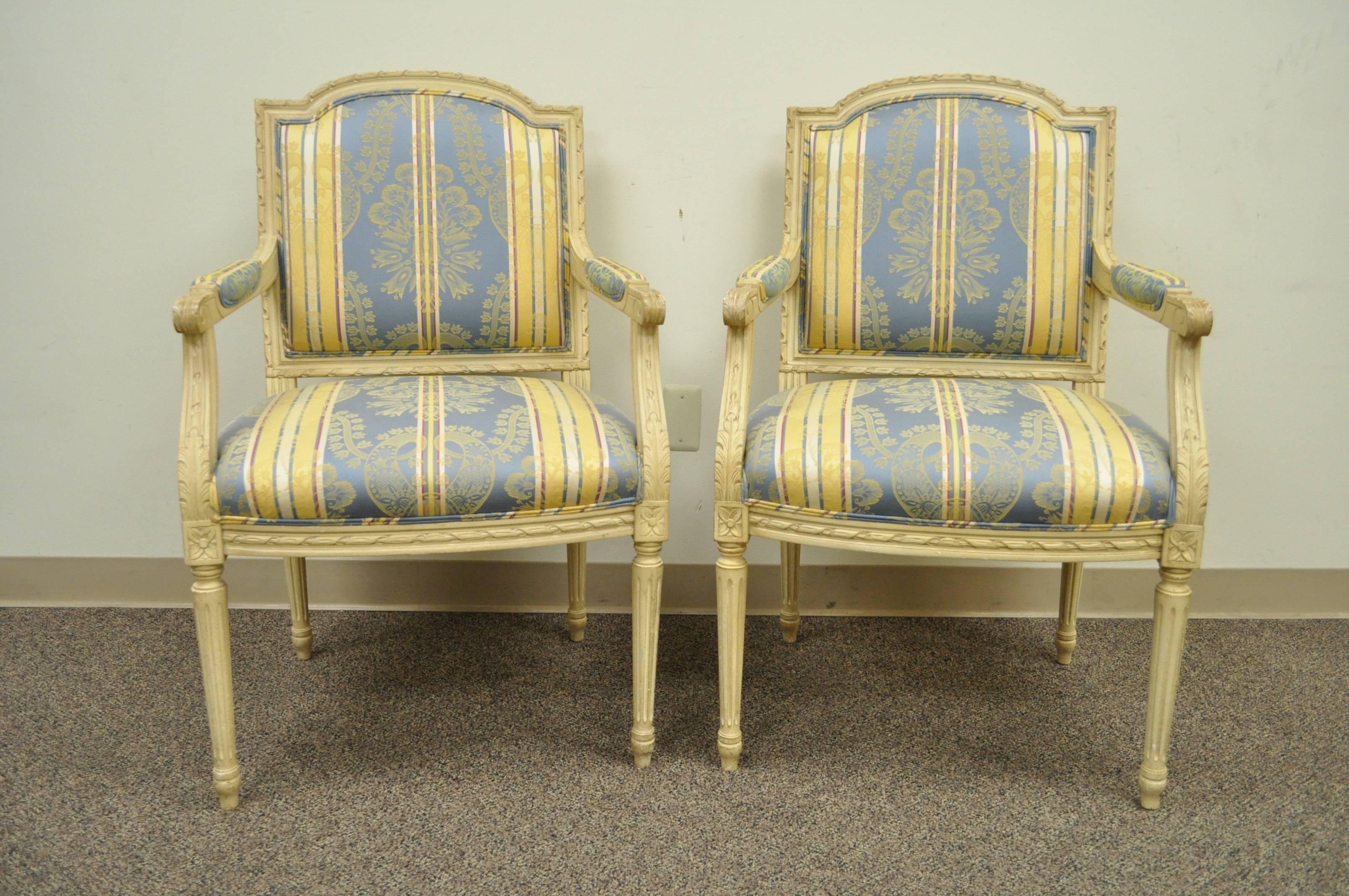 Pair of 20th century French Louis XVI style armchairs with finely carved floral and ribbon form accents, scroll form arms, and reeded and tapered column form legs. The chairs are upholstered in an absolutely lovely blue and yellow striped fabric