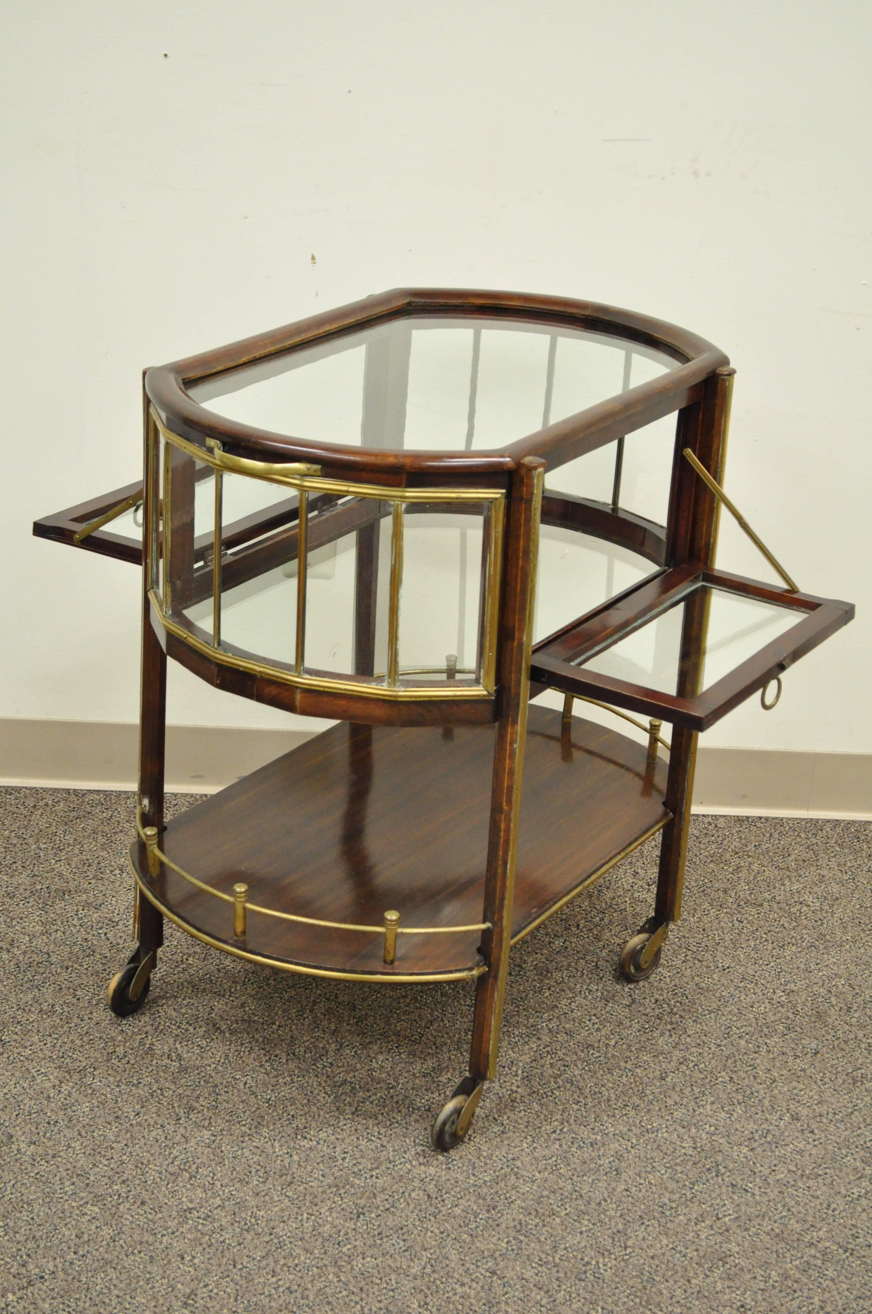 Very unique 19th century English mahogany and brass drop side rolling drinks trolley. Item features individual panes of glass on the top and all sides, two drop side doors. Clear glass interior surface, brass trim and gallery and unique wooden