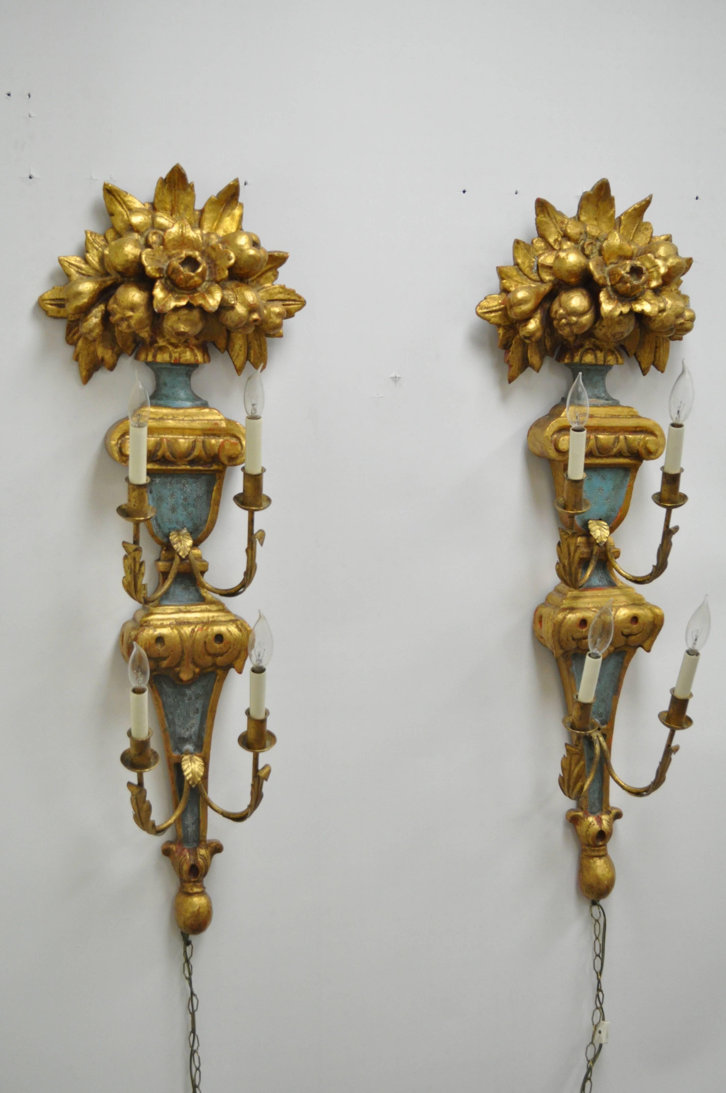 Pair of 1950s carved giltwood Italian style four-light wall sconces, made in Spain by Masa. Item features four iron arms each with four electrified lights, painted and gilt finish, carved wood floral and fruit bouquet toppers and stately size and