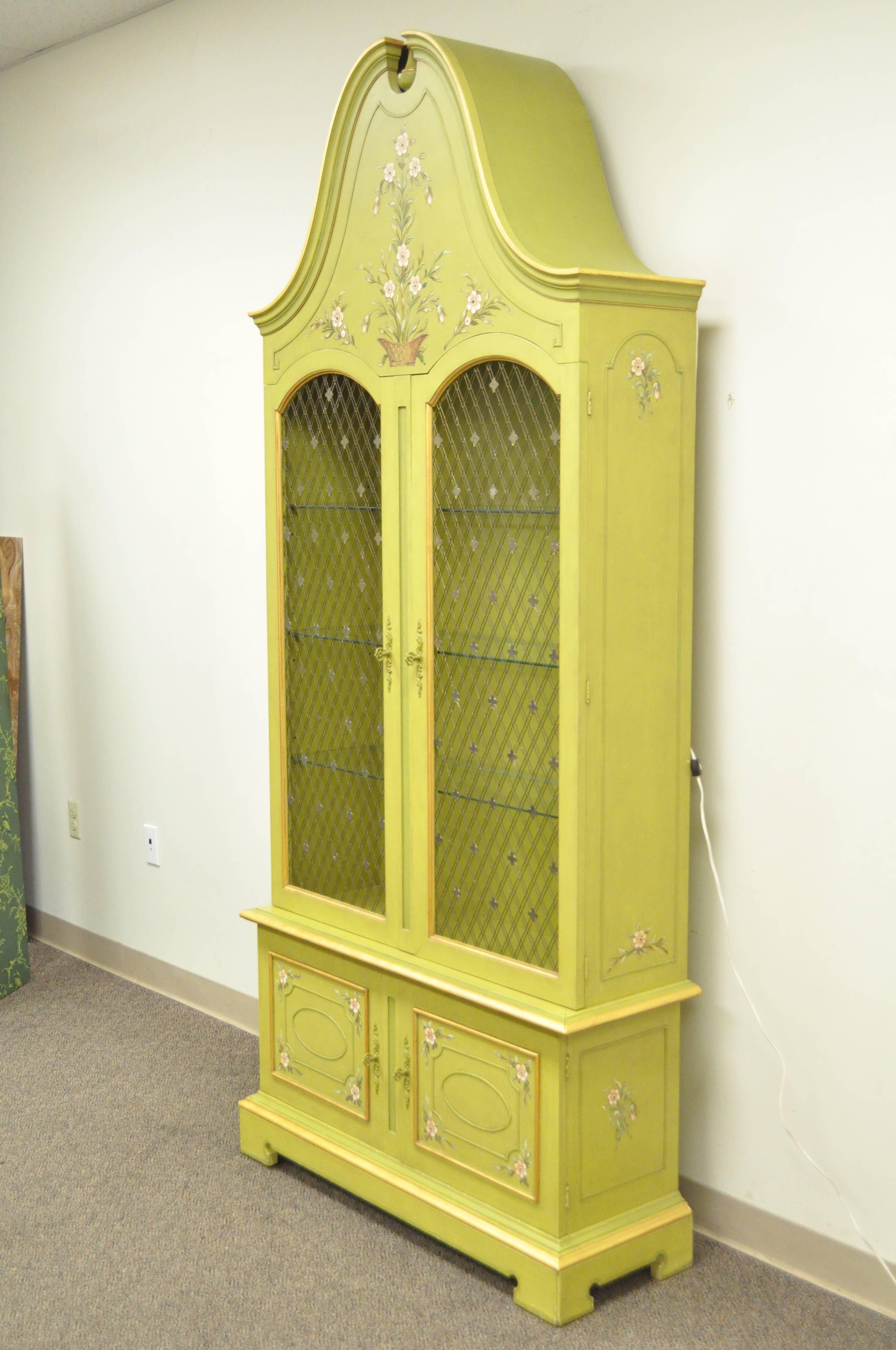 Two-piece hand-painted curio cabinet with elegant narrow form and dramatic dome/bonnet top by John Widdicomb. Item features gilt metal wire door inserts with quatrefoil mounts, illuminated interior, three glass shelves, hand-painted floral detailing