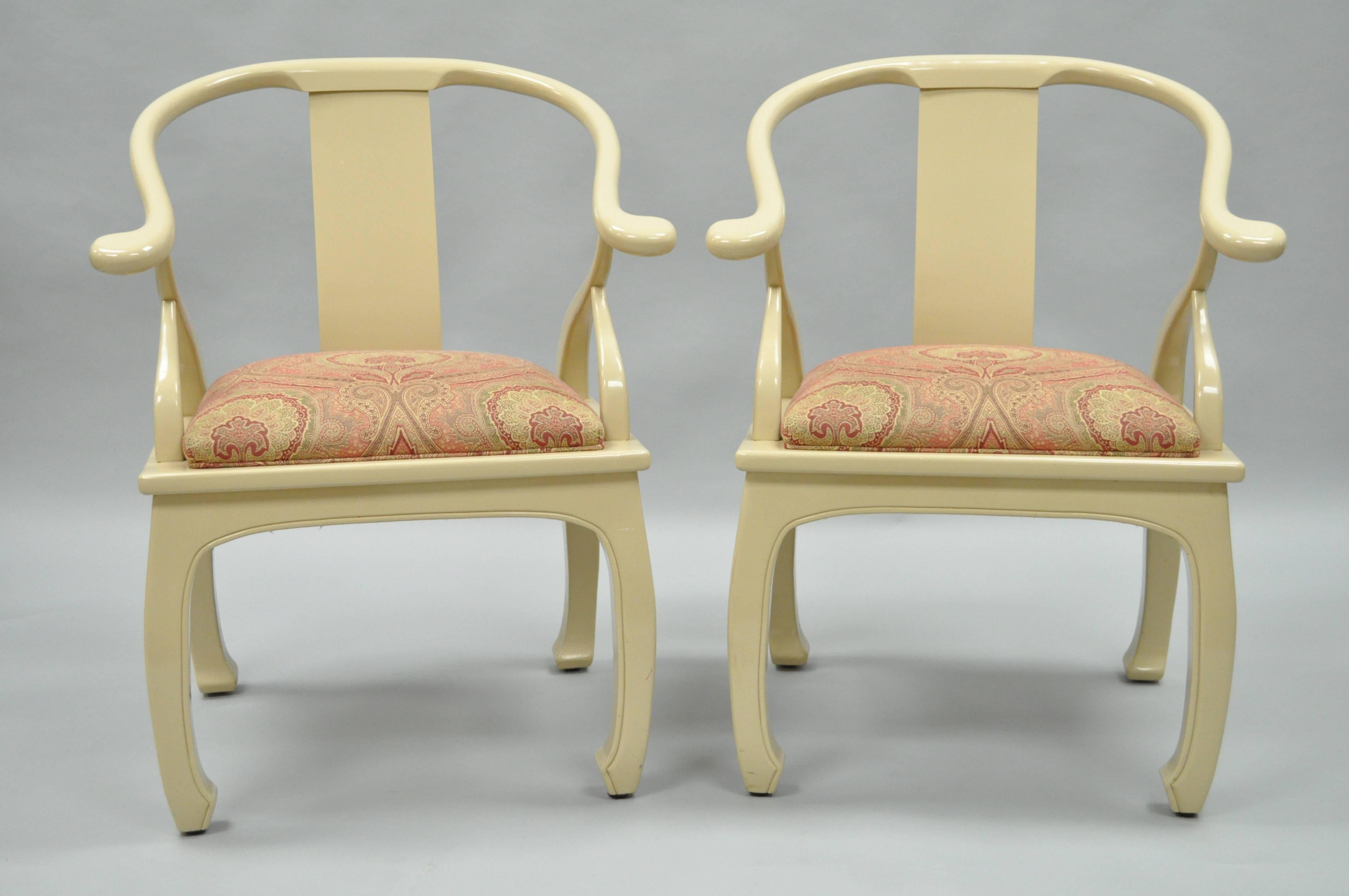 Quality pair of vintage decorator cream lacquered Asian inspired lounge chairs. The pair features solid wood frames, cream lacquered finish, horseshoe barrel backs, burgundy and gold upholstered seats, angled arm supports and classic Ming dynasty