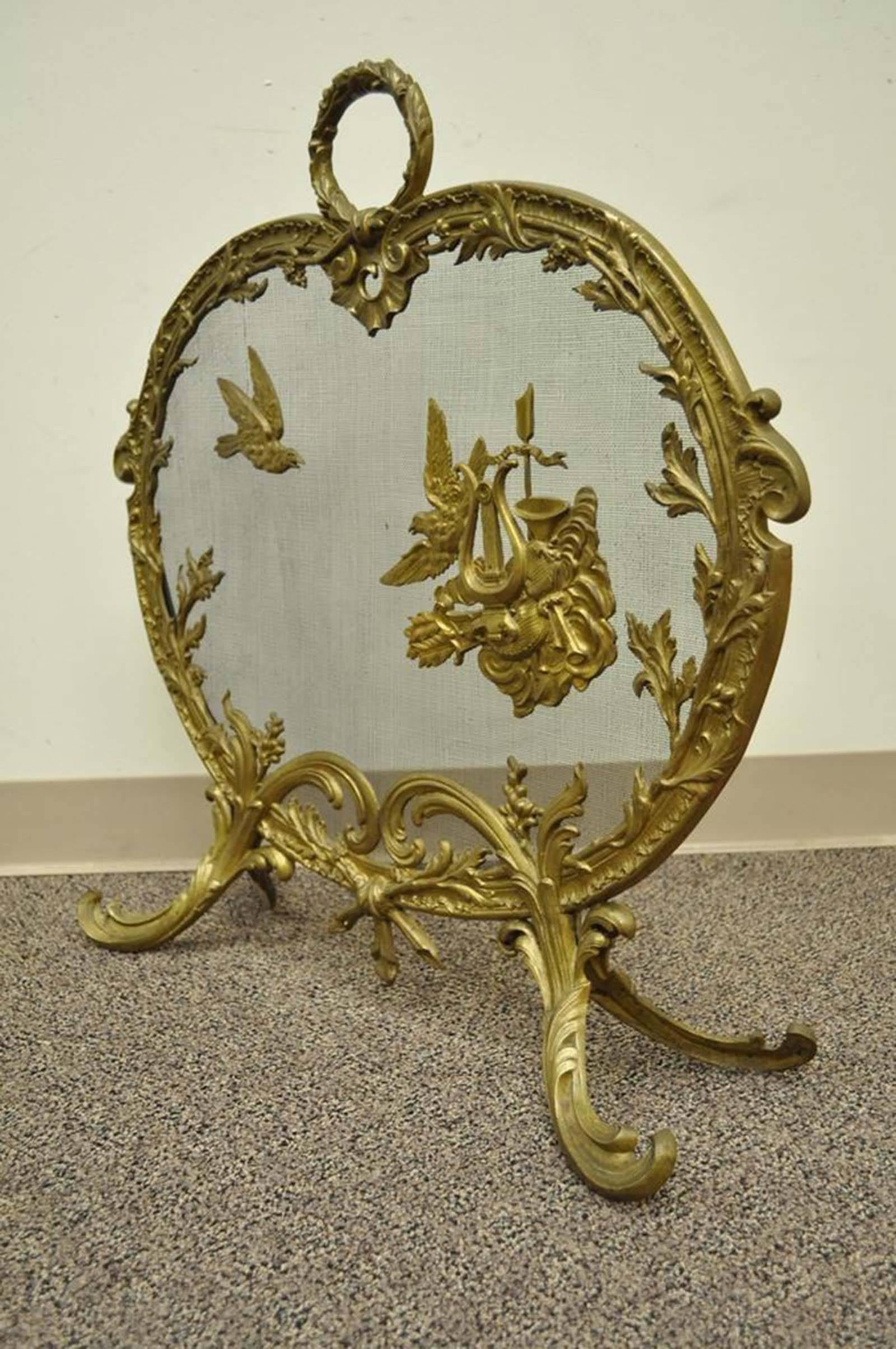 Gorgeous antique French Rococo/Louis XV style cast bronze fireplace screen. The screen is very ornate, with floral and scroll work borders, scrolled feet, wreath form handle, and two suspended birds, one of which is carrying several musical