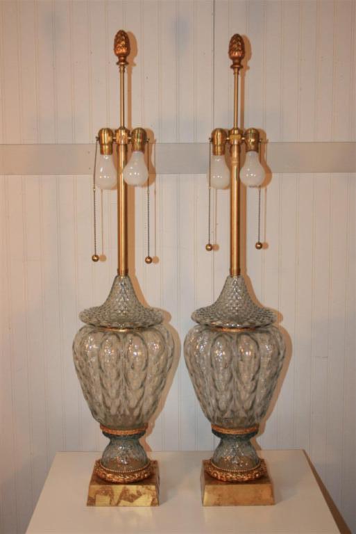 Very fine pair of large light blue tint crystal Murano glass lamps by Marbro featuring vase formed bodies, gold leaf bases, and brass ring foliage detail. Double socket, brass ball pulls, and large acorn finials all signature Marbro features. Price
