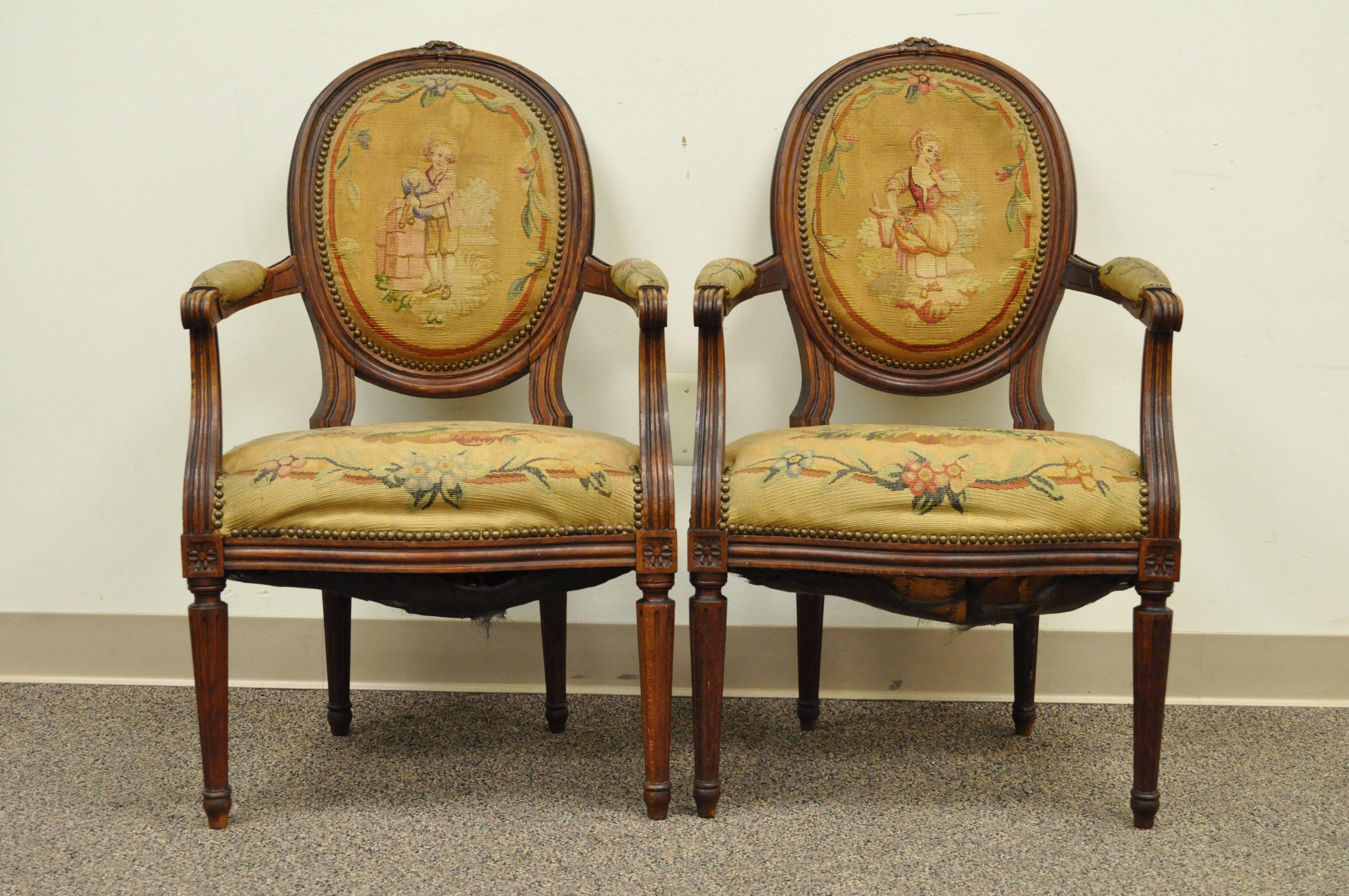 Pair of French 19th century Louis XVI style walnut armchairs with original needlepoint upholstery. Chairs feature padded arms, channel backs, bow carvings, fluted legs. Each chair has different needlepoint figures on the upholstered backs.