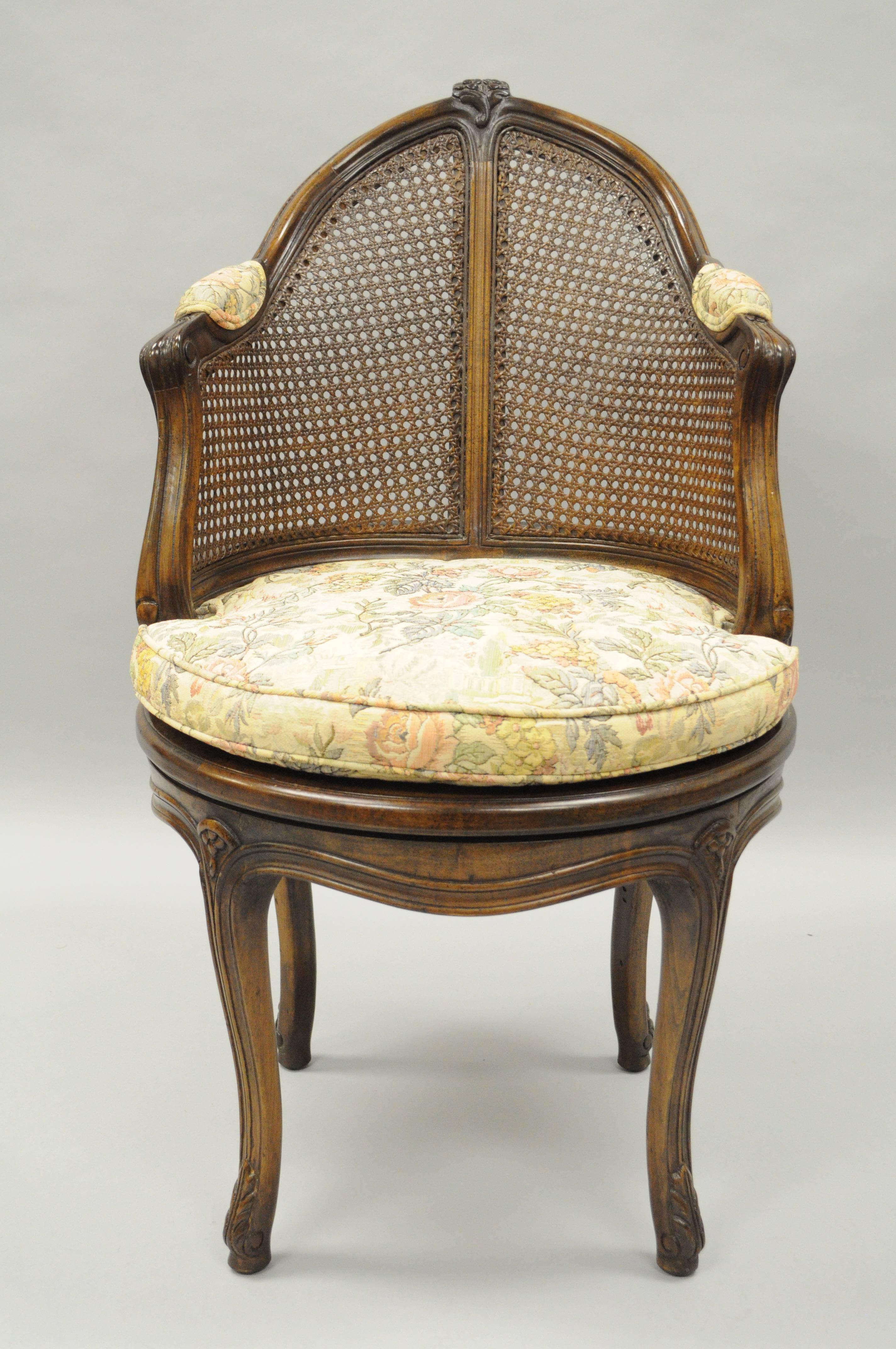 Vintage French Country / Louis XV style revolving vanity chair or stool. Item features a solid carved wood frame, shapely cabriole legs terminating at carved feet, cane back and seat, loose cushion, upholstered armrests, floral carved pediment and