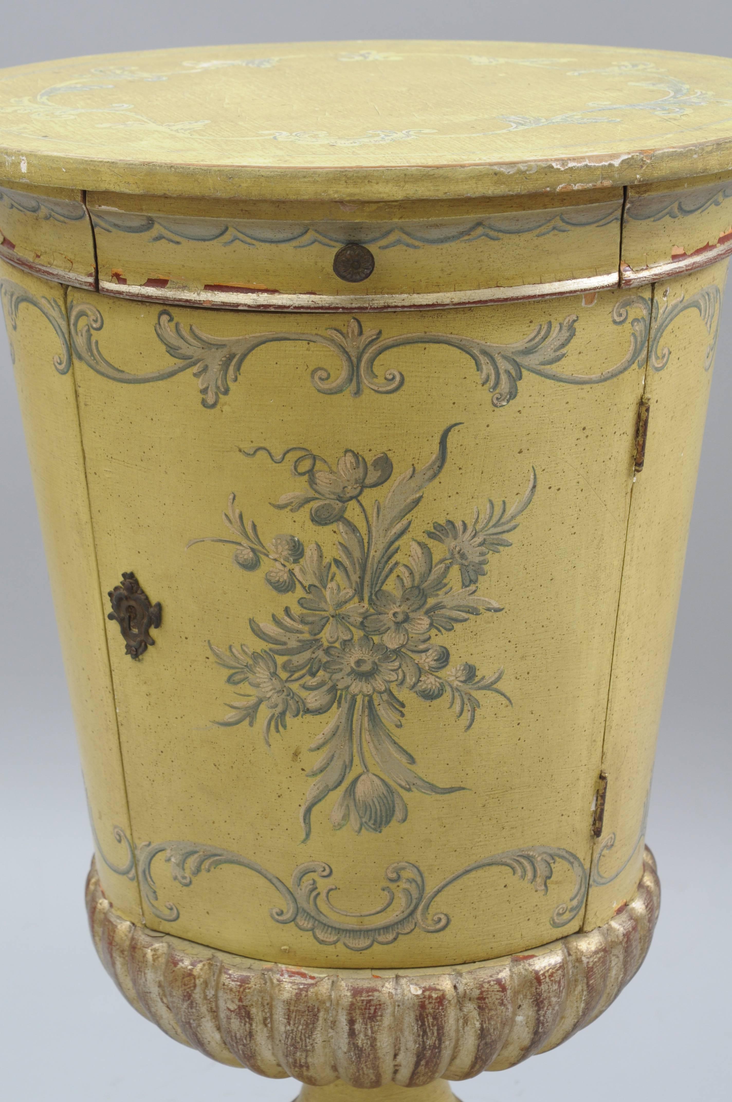 Antique Italian neoclassical style urn form side cabinet drum table. Item features a single drawer, lower swing door with working lock and key, blue hand-painted floral and acanthus leaf details throughout, round top, yellow finish, parcel silver