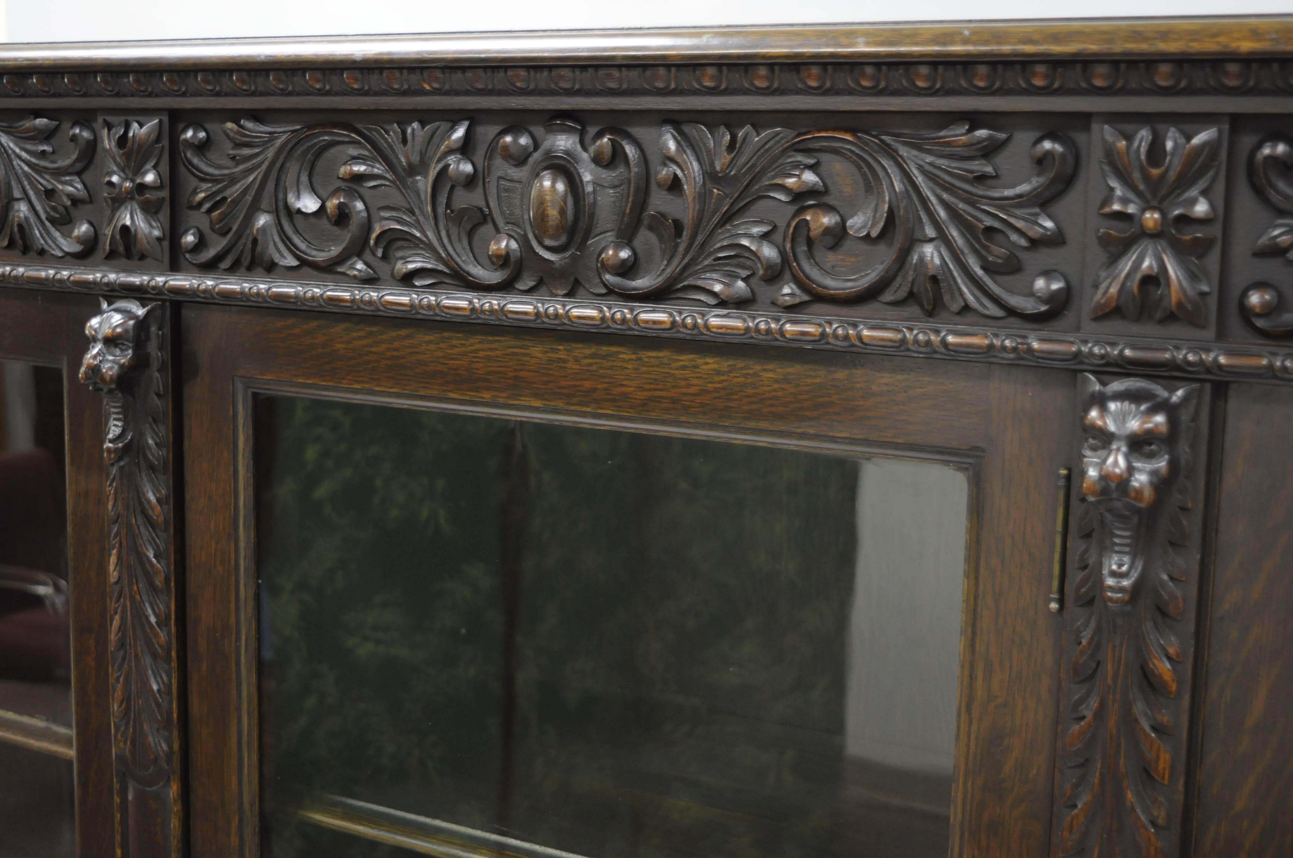 Exceptional antique Victorian oak three-door large triple bookcase with carved figural Gargoyle faces and paw feet. Bookcase features floral foliate and shield carvings across the top border, four open mouth gargoyle faces, four paw feet across the