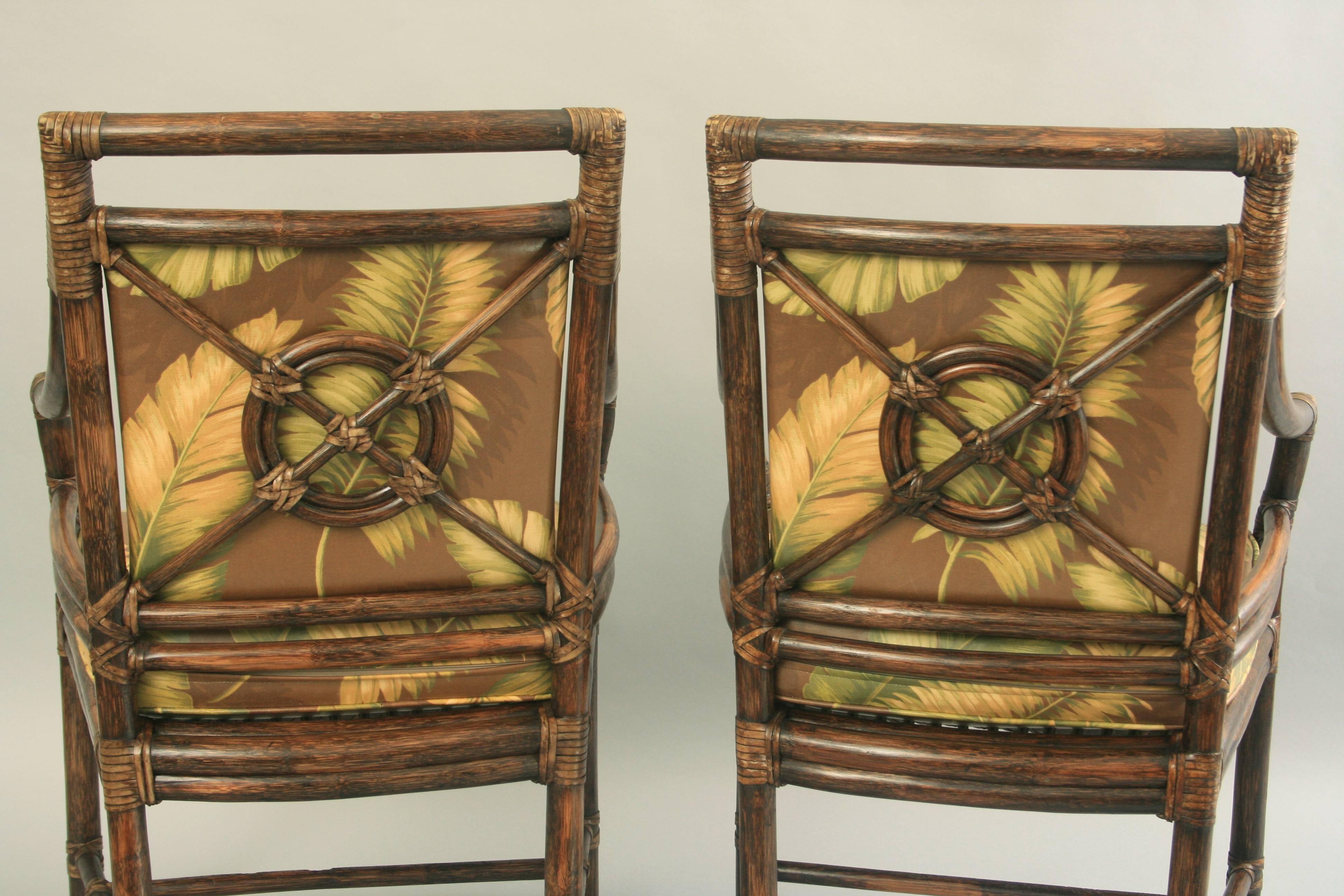 Pair of McGuire Rattan Target Back Arm Chairs. Chairs feature solid wood construction, rawhide corner wraps, target back, removable vinyl seat cushions with tropical palm print, original labels, great quality and form, circa mid-late 20th century.