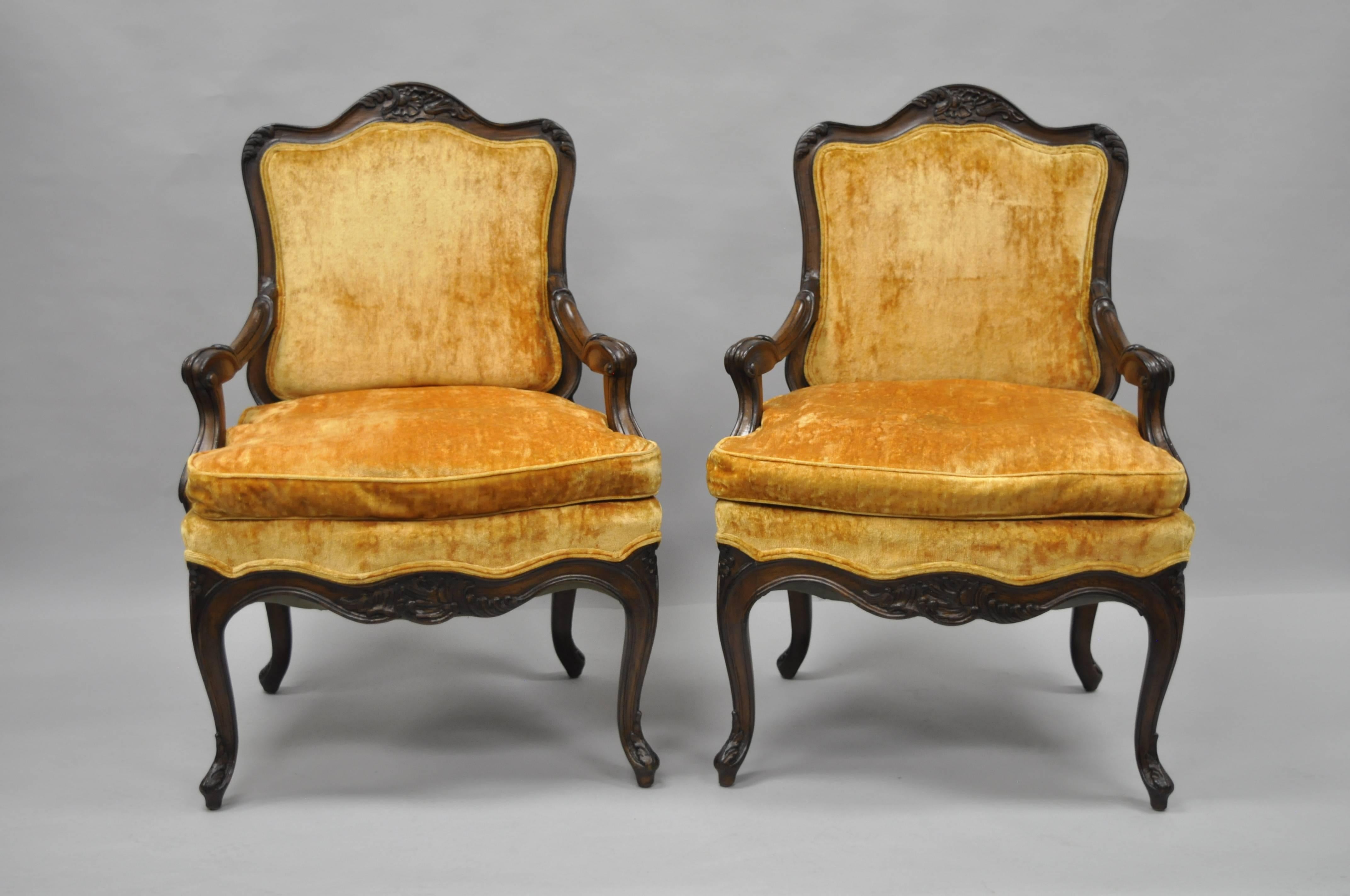 Pair of vintage country French/Louis XV style Hollywood Regency armchairs. Item features heavy solid wood frames, shapely rolled arms, cabriole legs, carved upper and lower rail, and a dark stained distressed finish. Measurements: 39