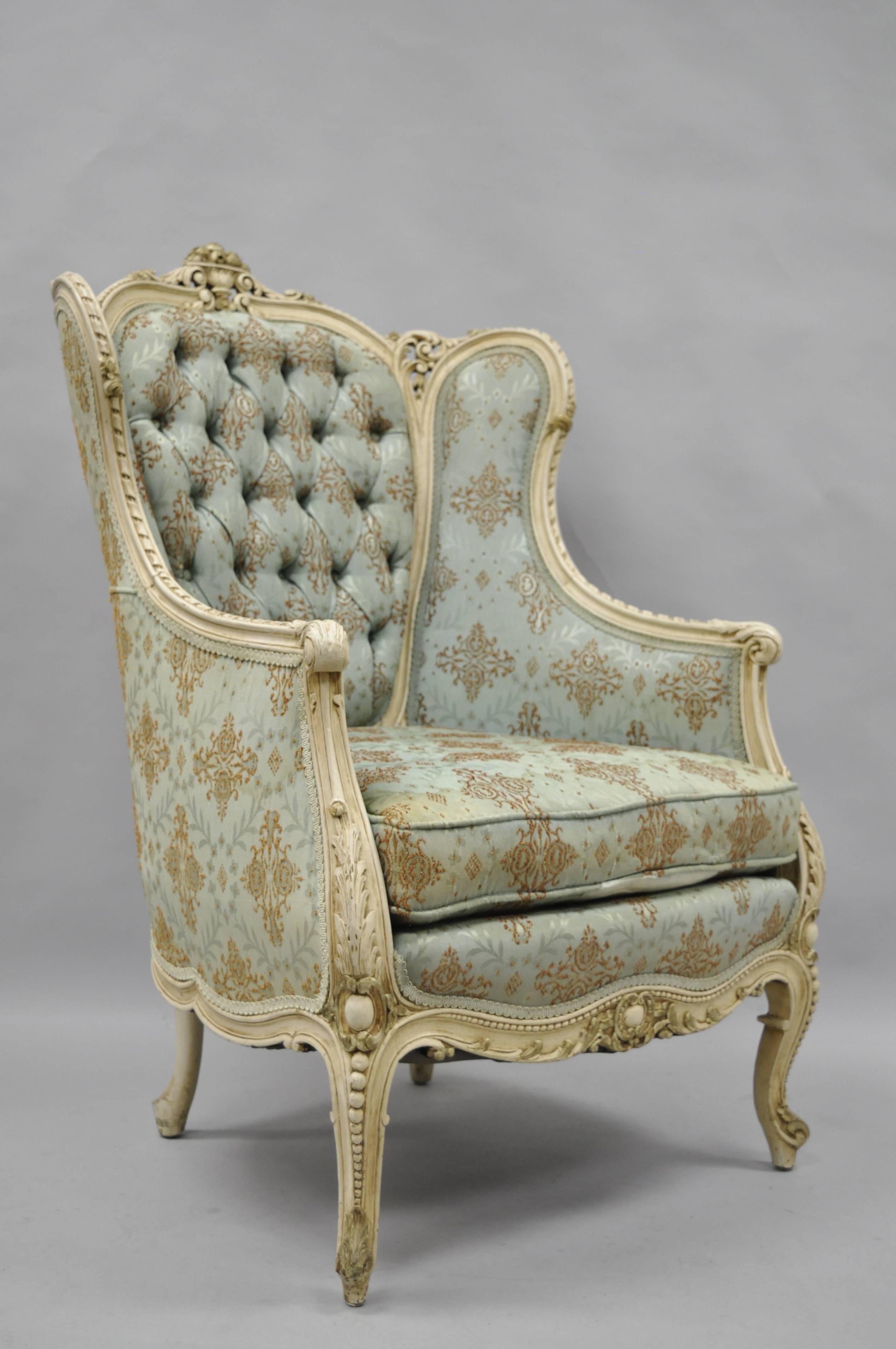 Early 1900s French Louis XV / Provincial Style Cream Painted Bergere Wing back Chair. Item features a solid carved wood frame, unique floral carved accents, cabriole legs, wing back, tufted fabric, cream painted distressed finish, and attractive