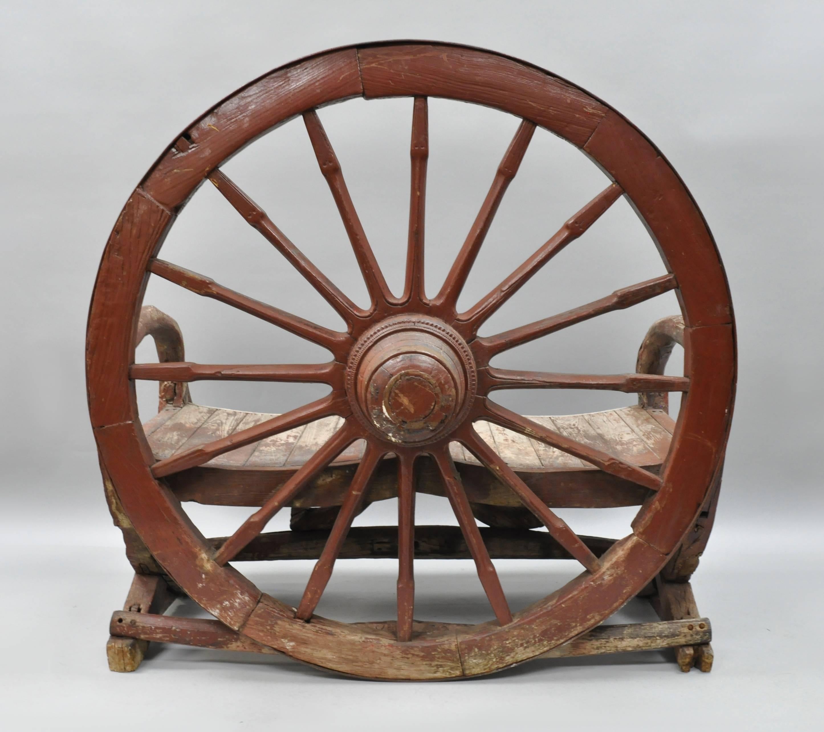 Antique primitive Conestoga wagon wheel red bench. Heavy solid wood and iron construction from an antique Conestoga wagon. Bench features the original distressed red paint, beautiful patina, two seat form, very impressive and unique item. Item