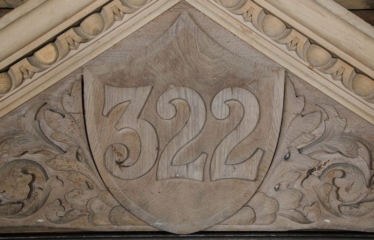 A large wooden door pediment in pine and beech. This carved overdoor or door pediment features well-defined egg and dart moulding with carved foliate decoration surrounding a central shield which displays the house number 322. This number could be