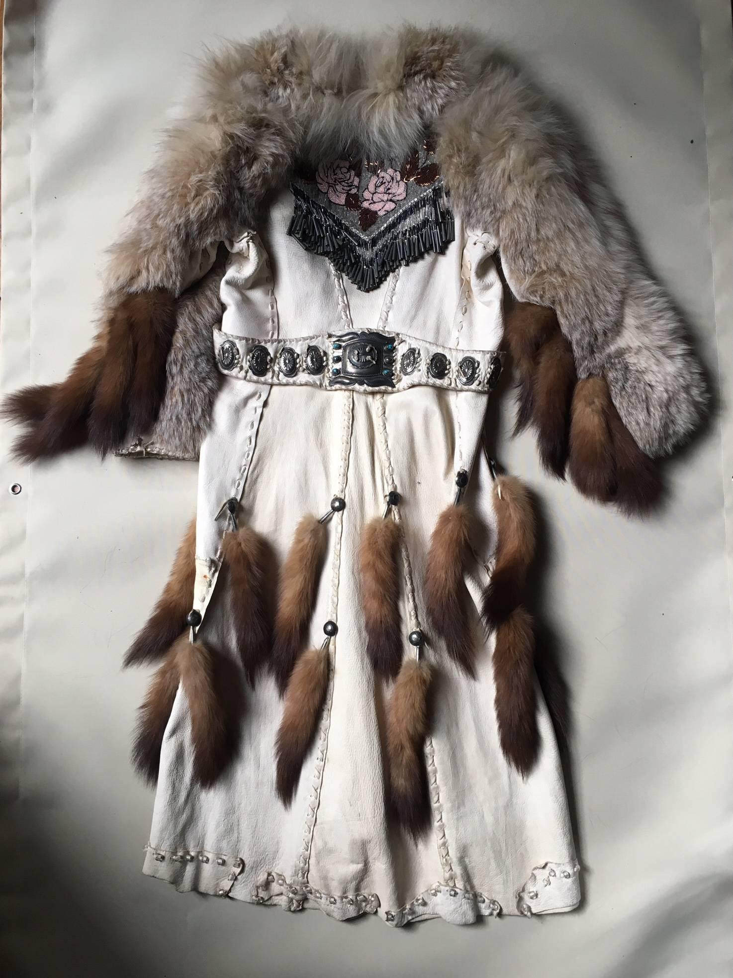 A large Cape in white patinated leather, ornated with wolf and fox fur, with rich beaded and embossed details, with an impressive belt of native Indian style with turquoise , bears a signature.
 