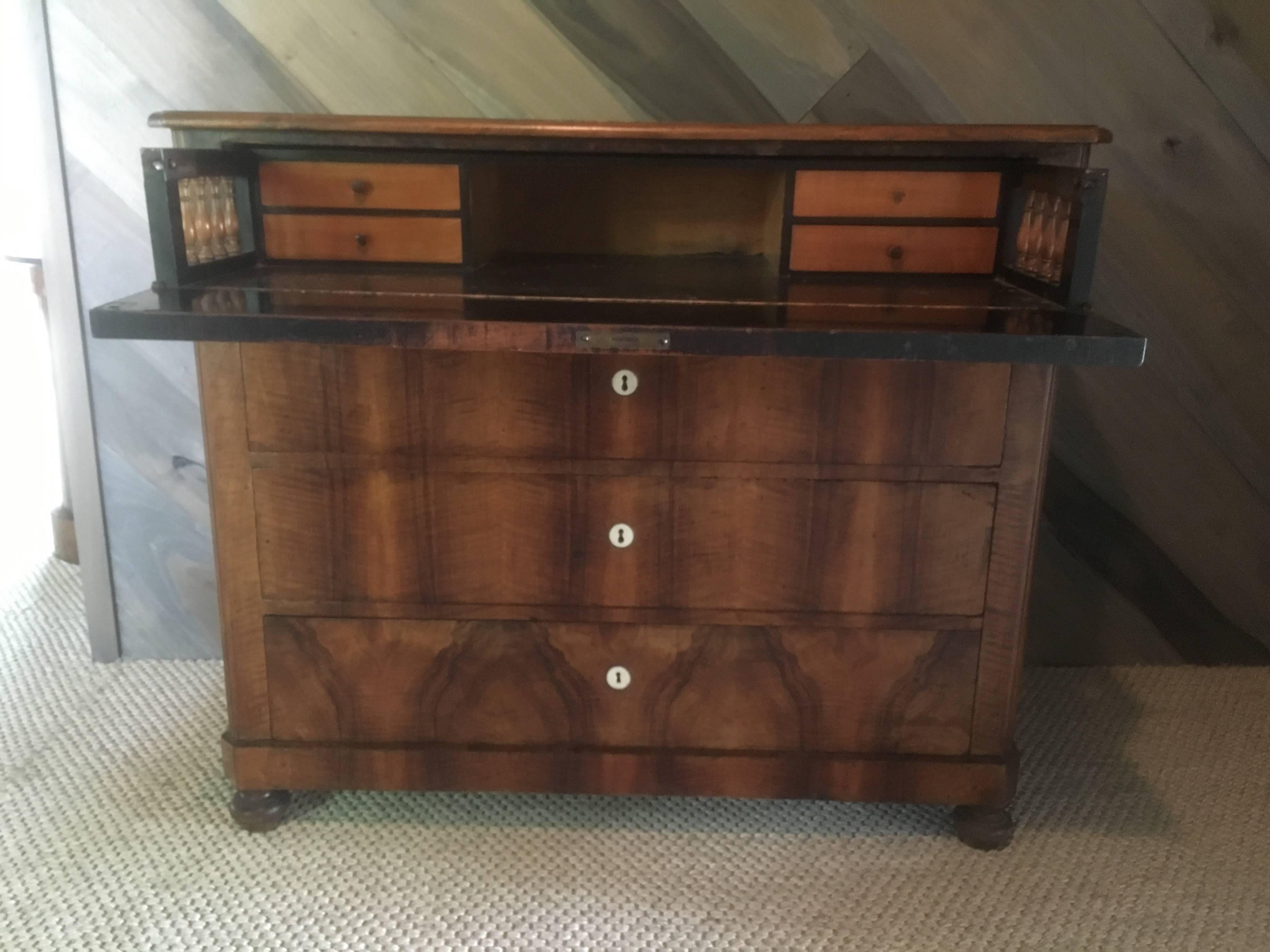 Biedermeier walnut four-drawer chest with bone escutcheons; the waterfall facade with single drawer over three long drawers in a matchbook walnut veneer. The top drop front reveals four ash drawers and ebonized wood with turned spindle column
