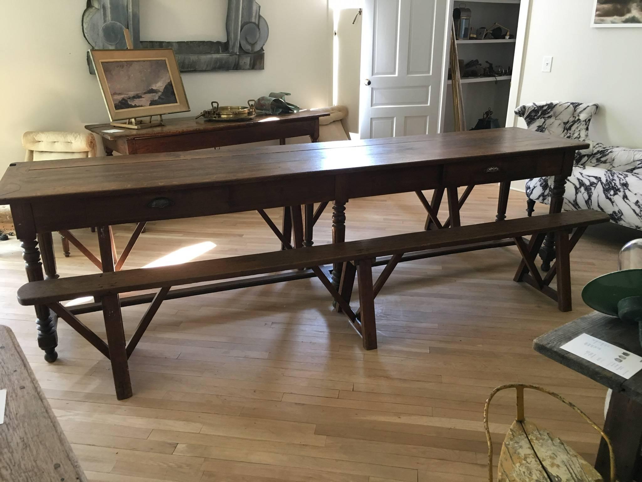 Very long French oak refectory table with center stretcher and two trestle benches. Beautiful patina, lines and craftsmanship. Two drawers with original carved metal cup pulls. At the end of the table is a steel reinforced notch and hook possibly