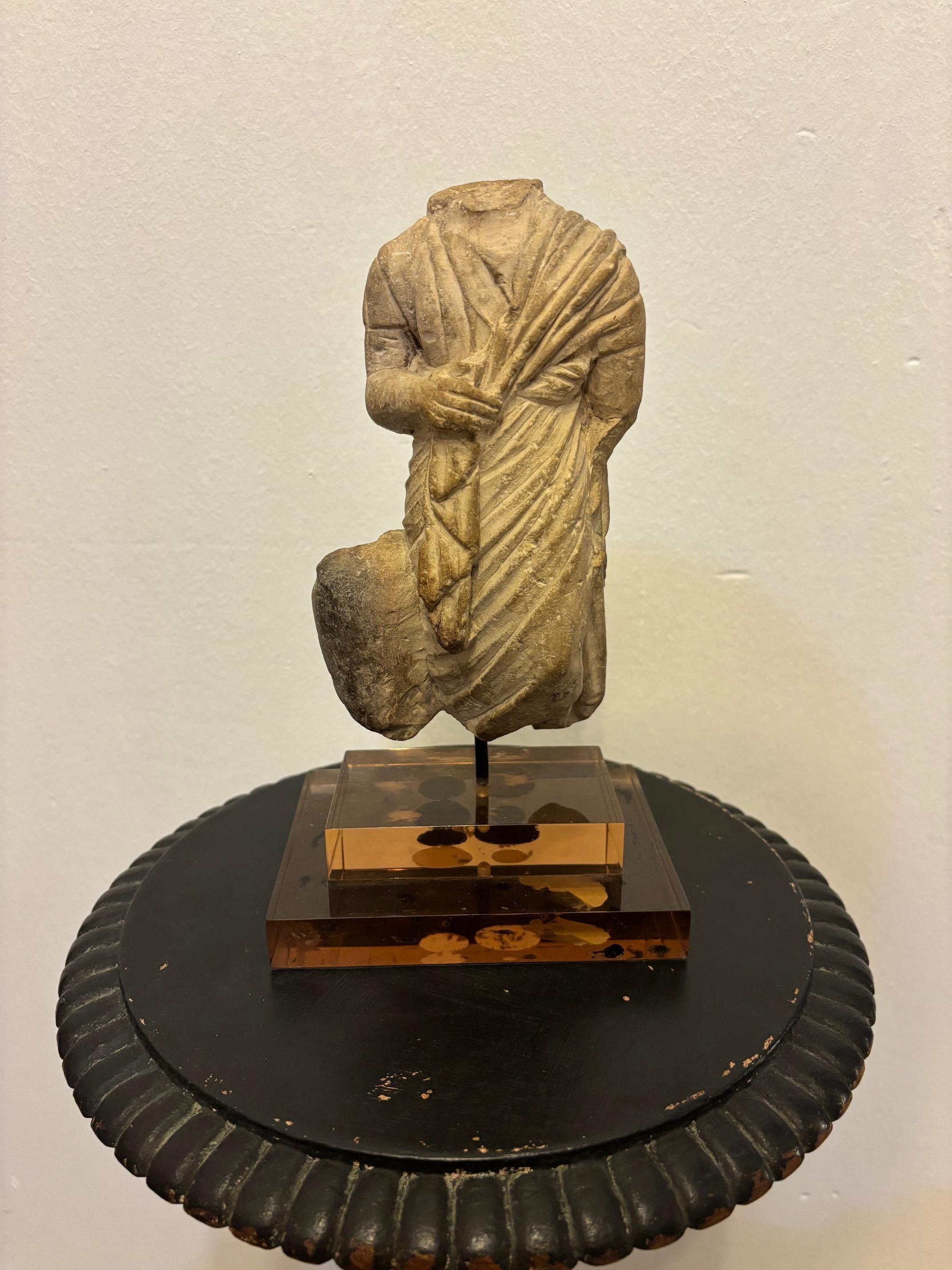 STATUETTA TOGATUS
Raffigurazione di una figura maschile vestita con toga e himation, sorretta dalla mano destra.
Presenza di un puntello sulla coscia destra, che implica che questo frammento faceva parte di un gruppo statuario.
Marmo. H. 23,5 cm
