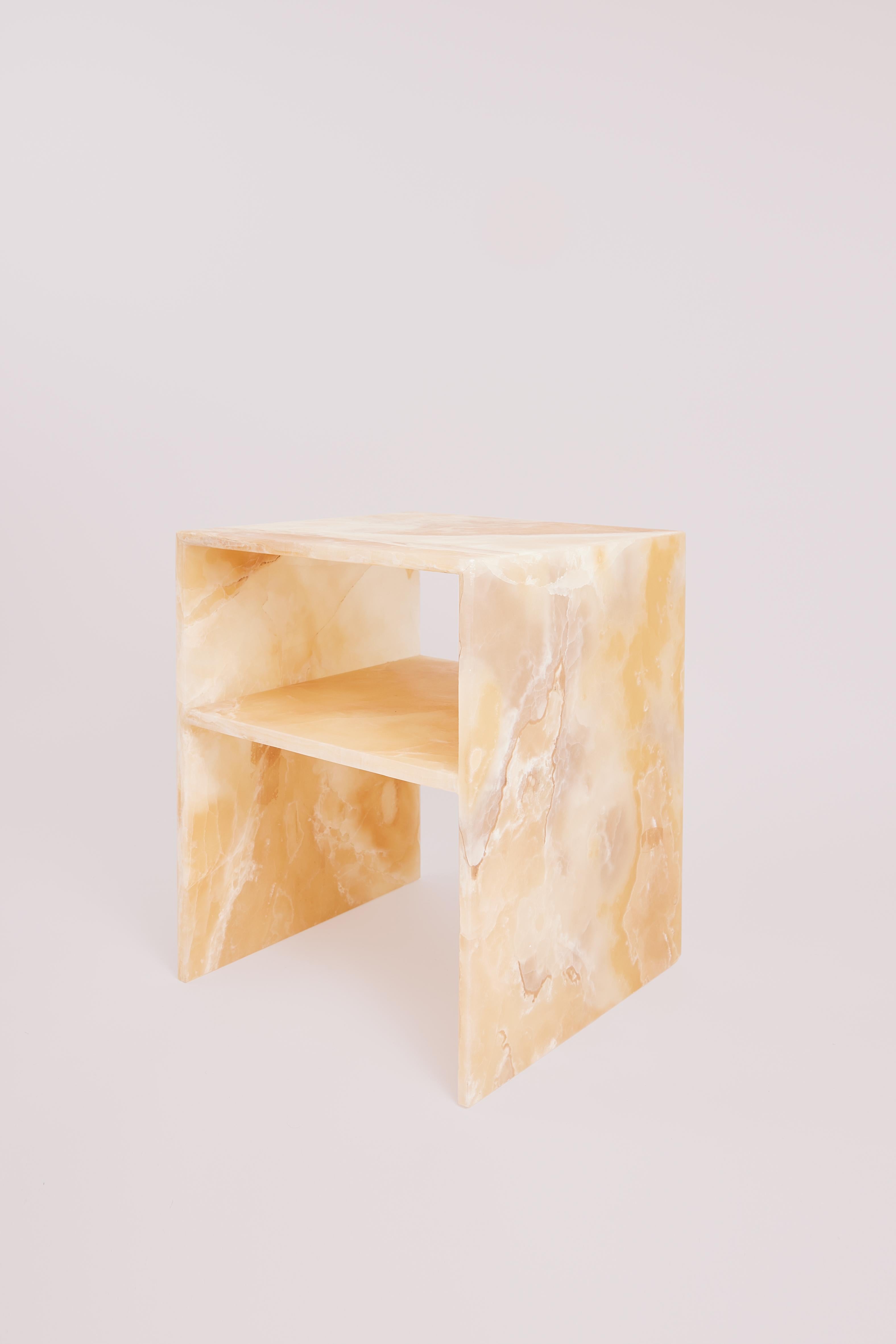 This sculptural bedside table by Studio Gaïa is carved entirely from Mexican amber onyx, a rare and precious stone known for its luminous depth and natural variation. With its distinctive honey, ivory, and warm caramel tones, the stone reveals