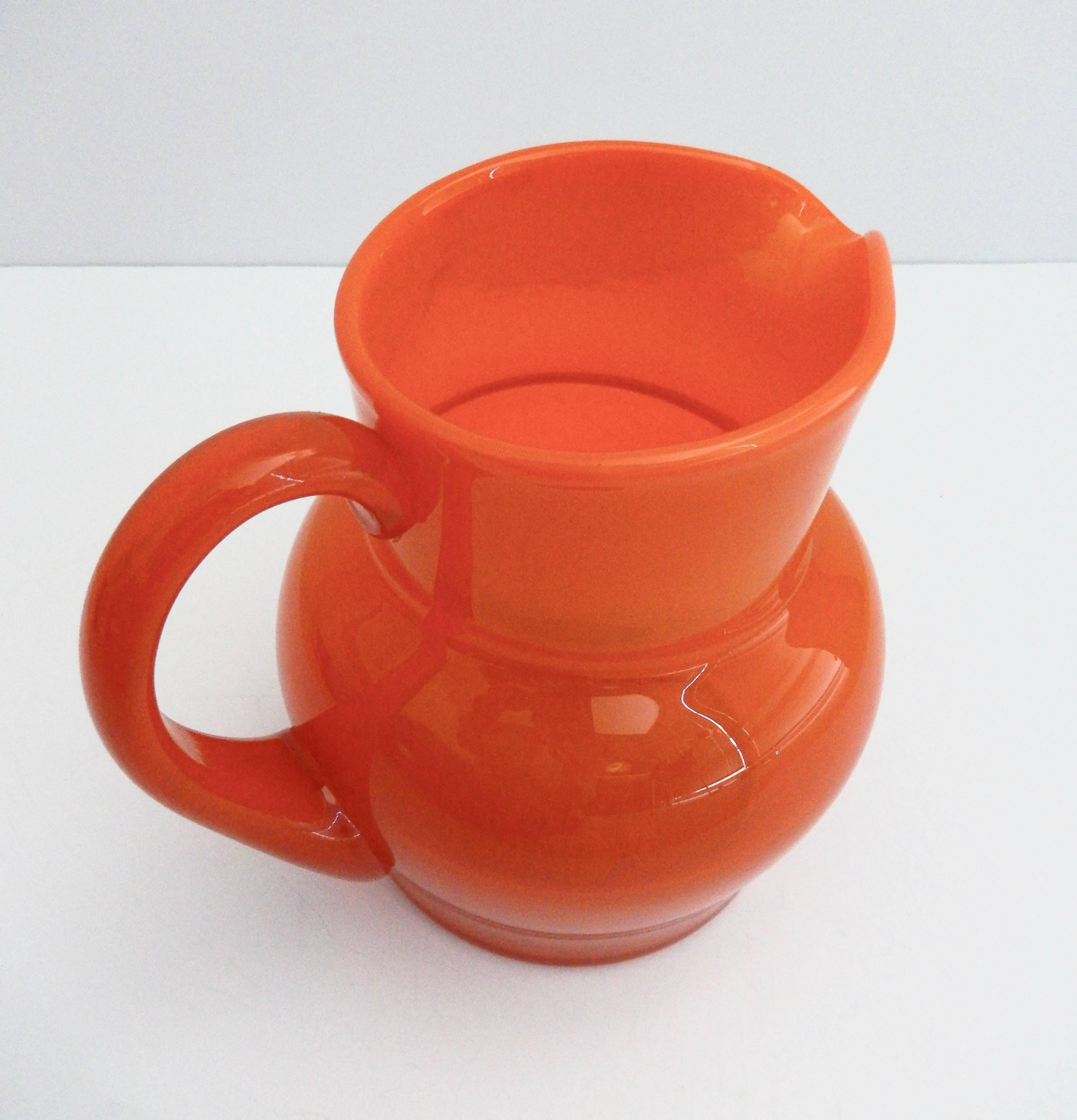 A blown-glass pitcher in tangerine orange by the Swedish artist Erik Hoglund (1932-1998). From 1953-1973 Hoglund designed for Boda. (The company name was changed to Kosta Boda in 1976.) Etched signature: H 1588/100 and original paper BODA