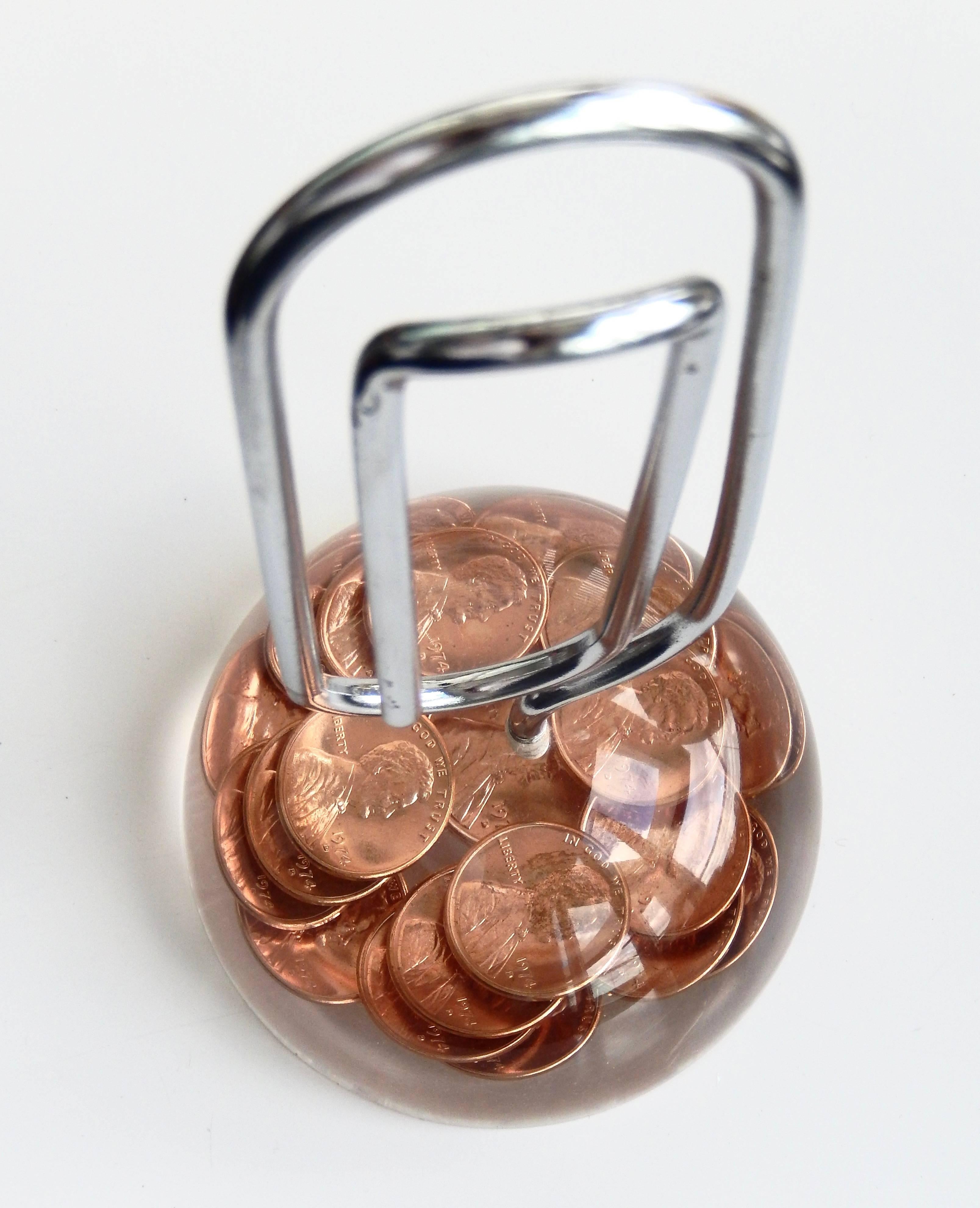 A large vertical paper clip embedded in a  domed lucite base displaying a design of 1974 copper pennies. Could it be commemorating the resignation of President Nixon? An interesting, well- made and functional desk accessory.