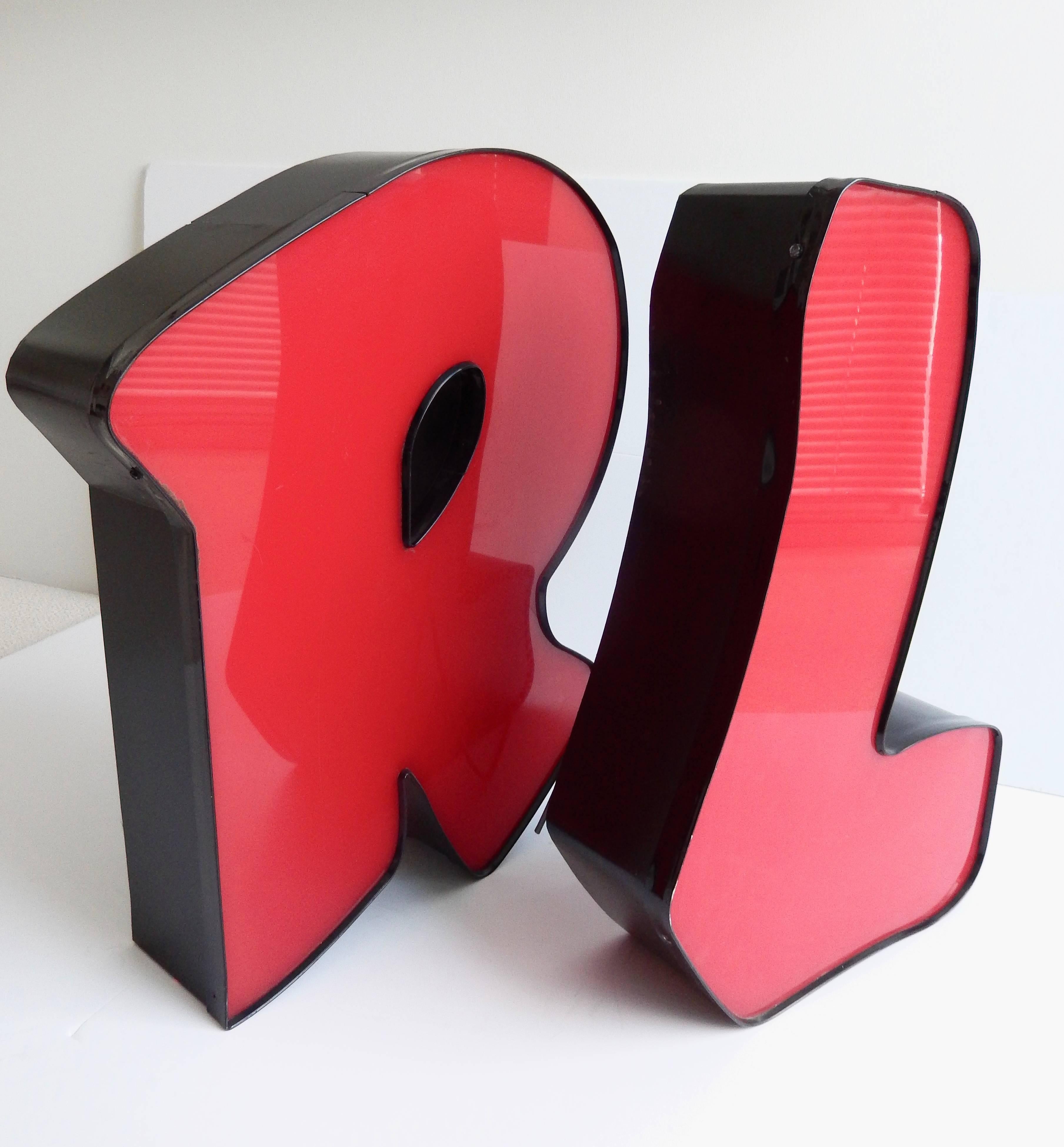 A pair of large cherry red acrylic letters in a friendly font reminiscent of comic sans. Both are freestanding, 