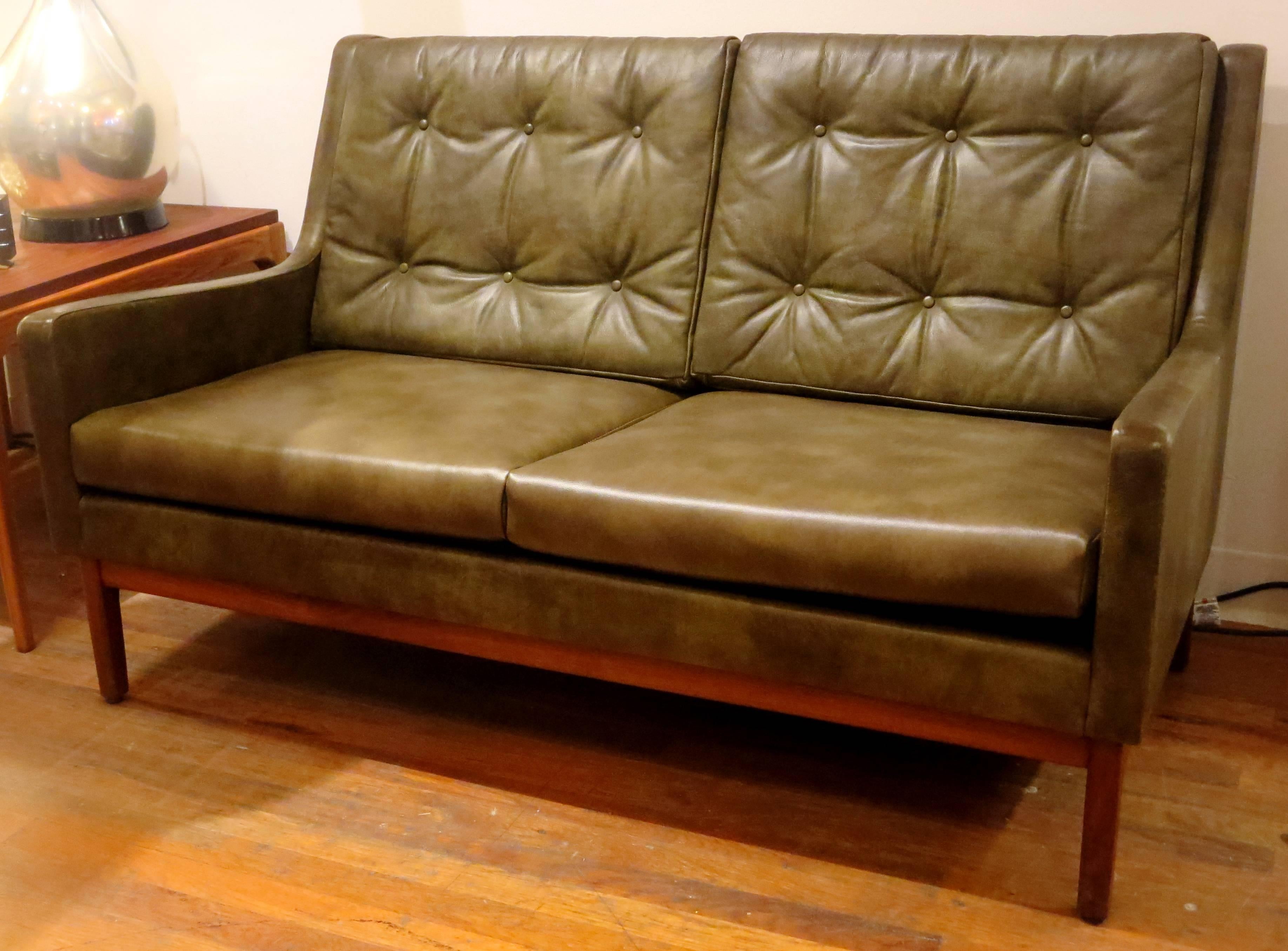 A very rare 1950s American modern loveseat by Gunlocke, in olive green leather, with tufted back cushions and solid walnut base frame, all in original condition, nicely worn some scuffs and marks on the back corners and upper top as shown, the base