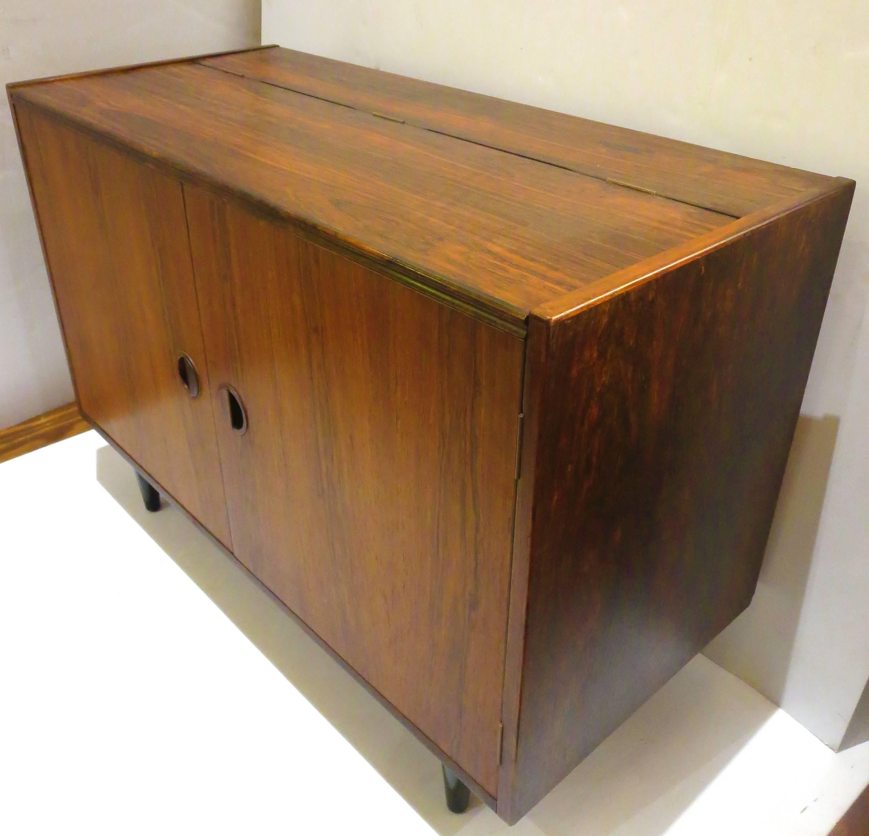 Versatile small double-door storage cabinet in rosewood, circa 1950s with removable shelves inside, and lift top, can be used as a mini bar. Nice condition black lacquer taper legs.