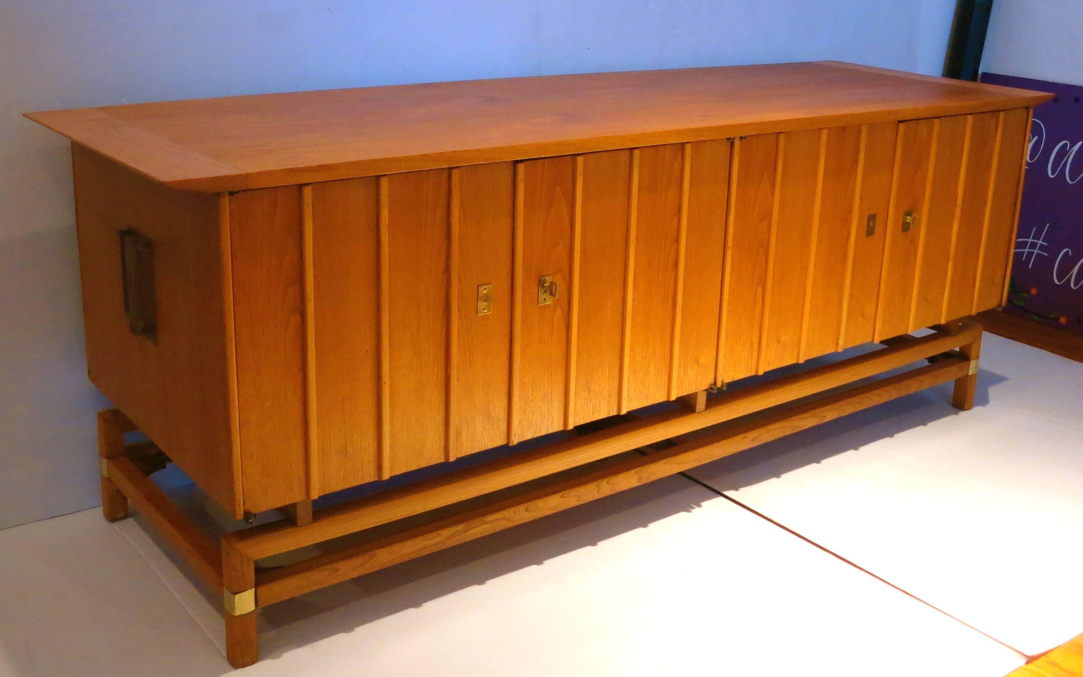 Beautiful Asian inspired low and long credenza, circa 1950s freshly refinished, with brass accents double cabinet door and single drawer on each side, with a light walnut finish.