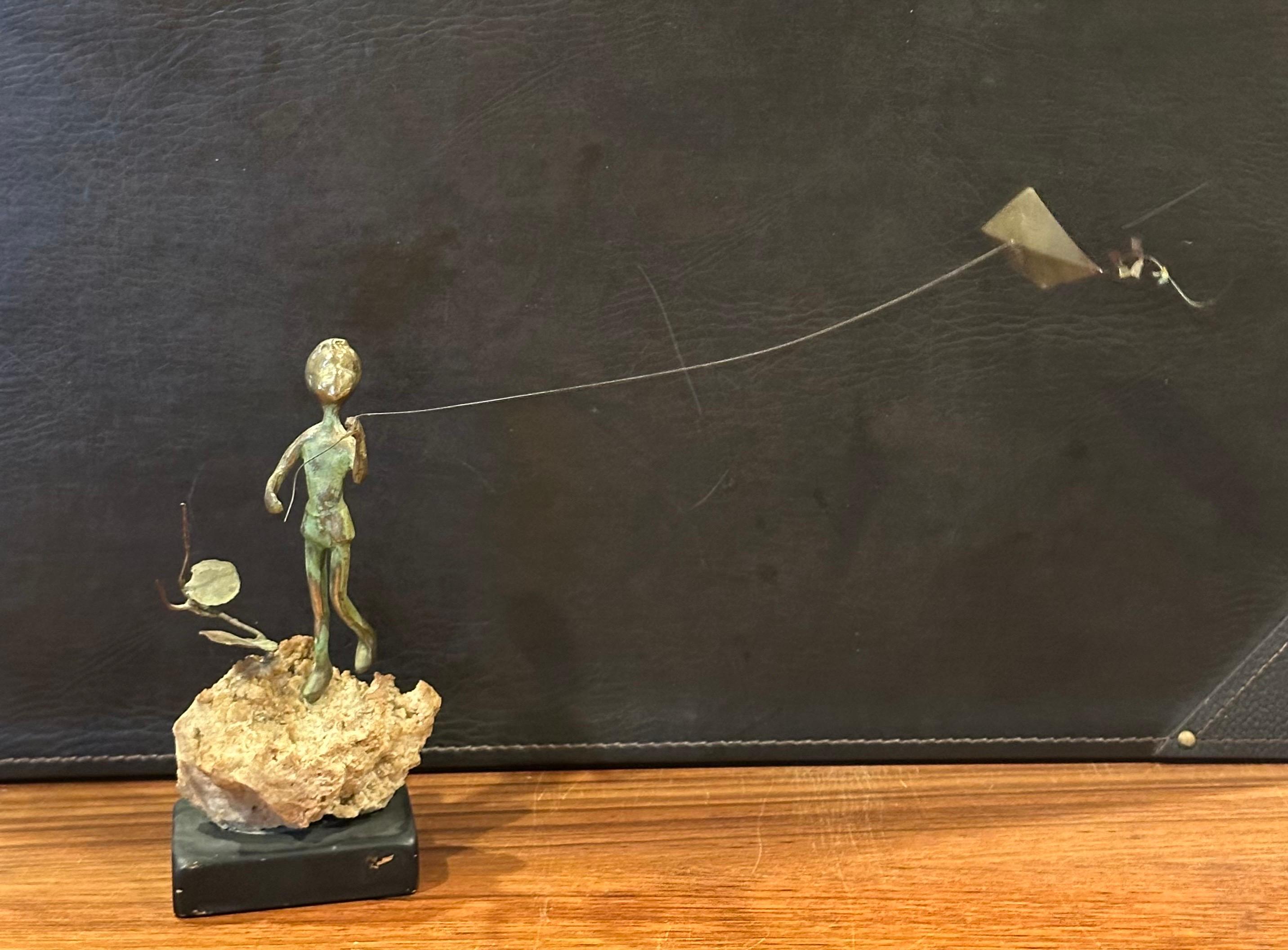 Una escultura de bronce de un niño volando una cometa sobre una roca volcánica, obra de Malcolm Moran, hacia la década de 1970. La pieza está en muy buen estado vintage y mide 10
