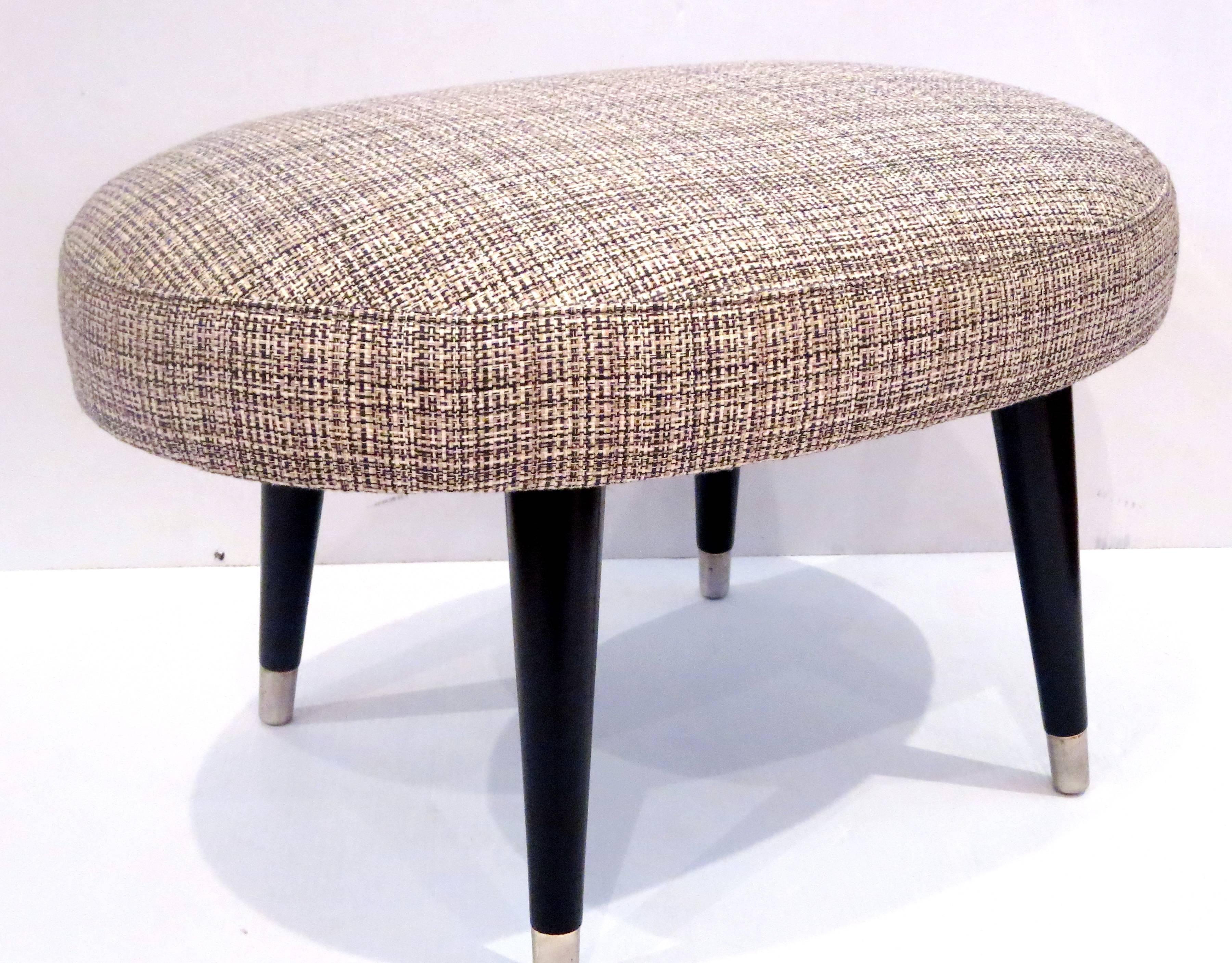 Excellent Mid-Century footstool has an elongated oval cushion and black lacquered legs. Upholstered in black and white tweed. Fully refinished and in excellent condition.