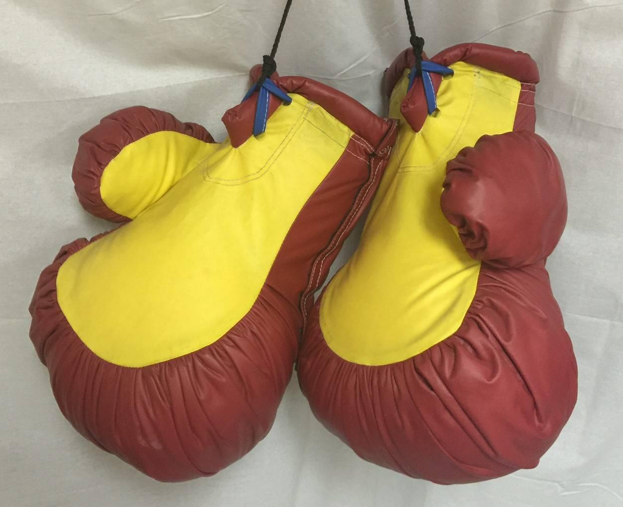 A very unique and eclectic pair of vintage over sized boxing gloves. Made of high quality red and yellow two-tone vinyl. Possibly used as a promotional item, they can be worn on each fist via a bar inside each glove.